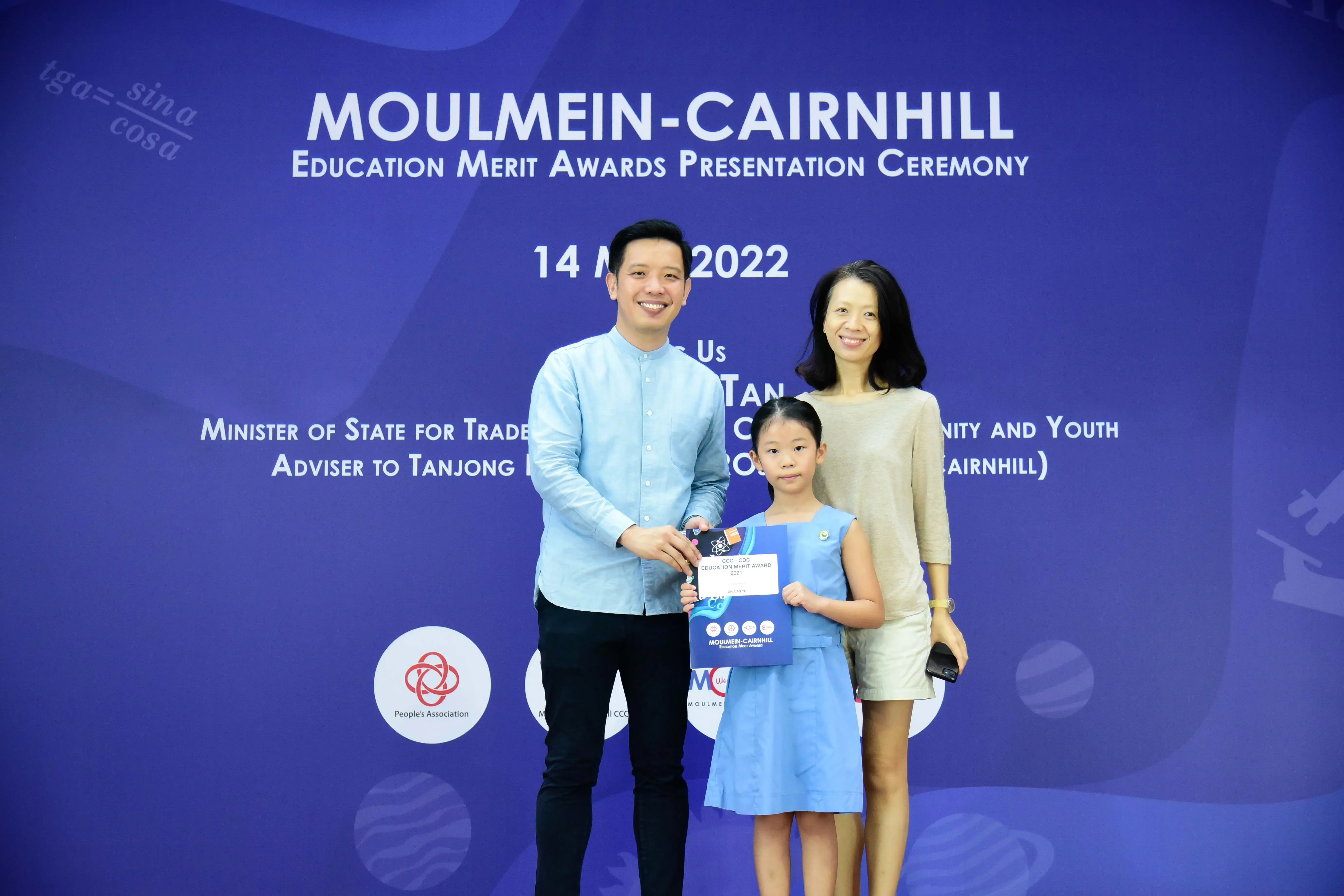 A man and woman stand with a young girl holding an award certificate at the Moulmein-Cairnhill Education Merit Awards 2022.