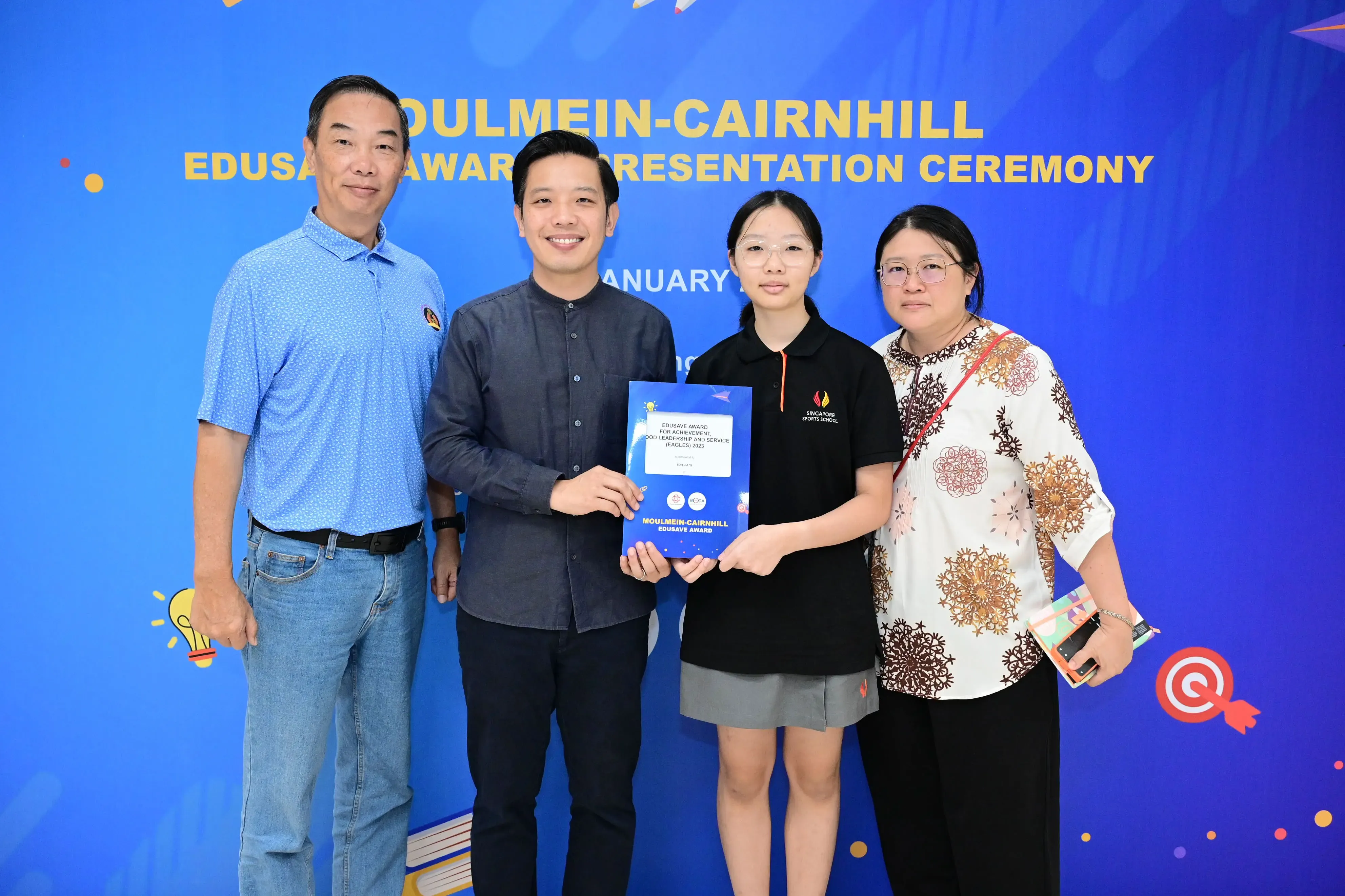 Four people pose at the Moulmein-Cairnhill Edusave Award Presentation Ceremony, with two holding a blue award certificate.