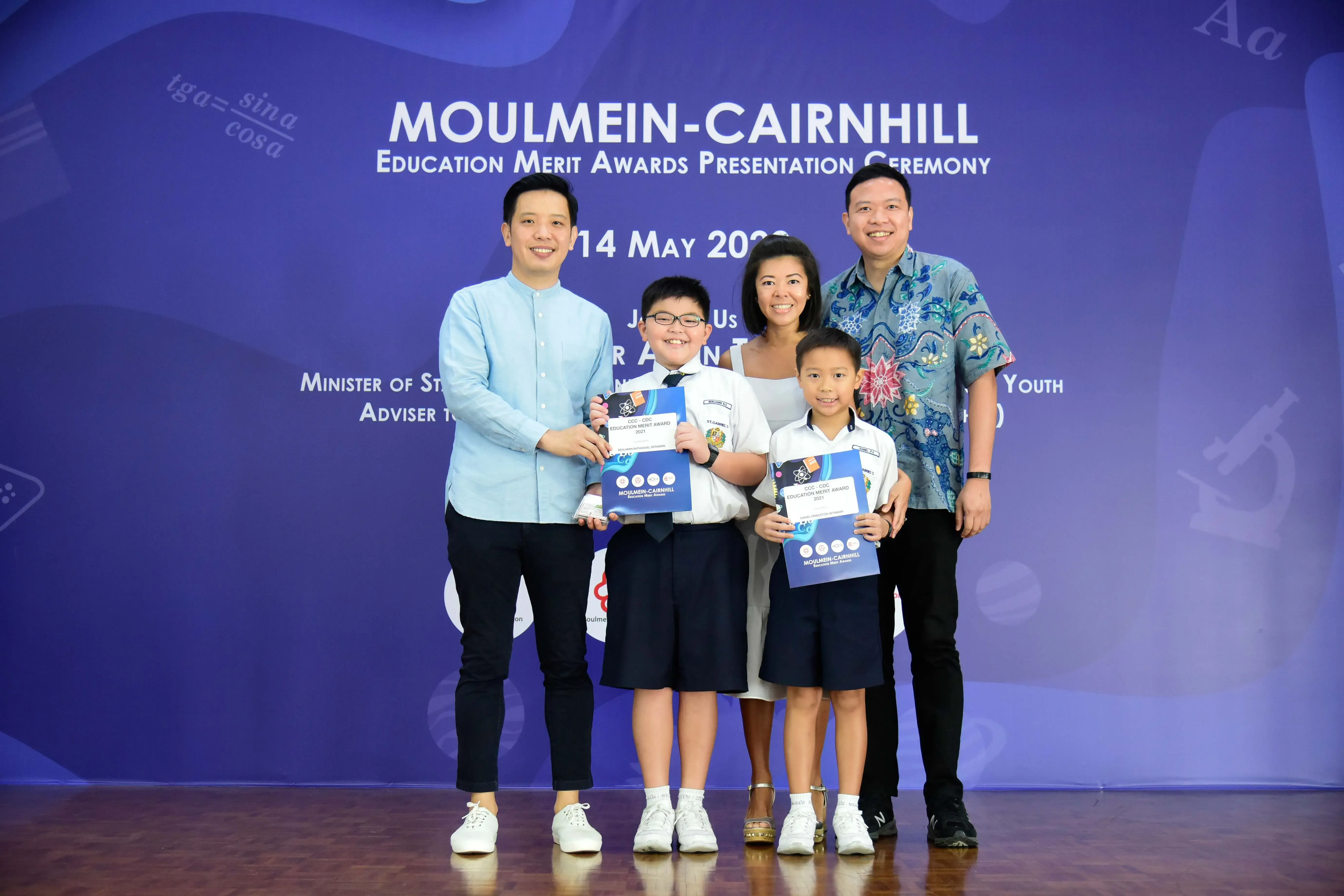 Two adults and two children holding award certificates at the Moulmein-Cairnhill Education Merit Awards Ceremony.