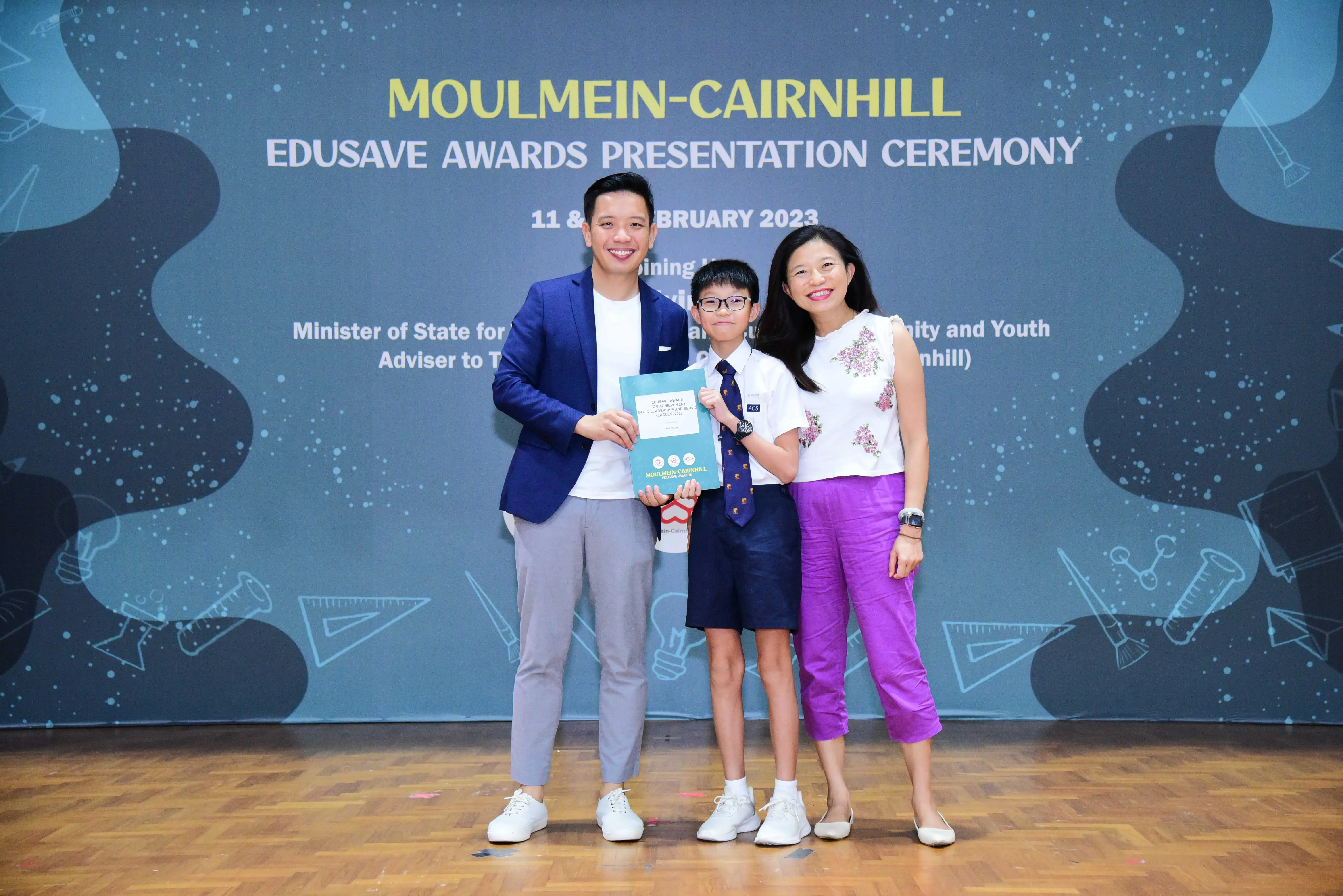 Two adults and a uniformed boy holding a certificate pose at the Moulmein-Cairnhill Edusave Awards Ceremony 2023.