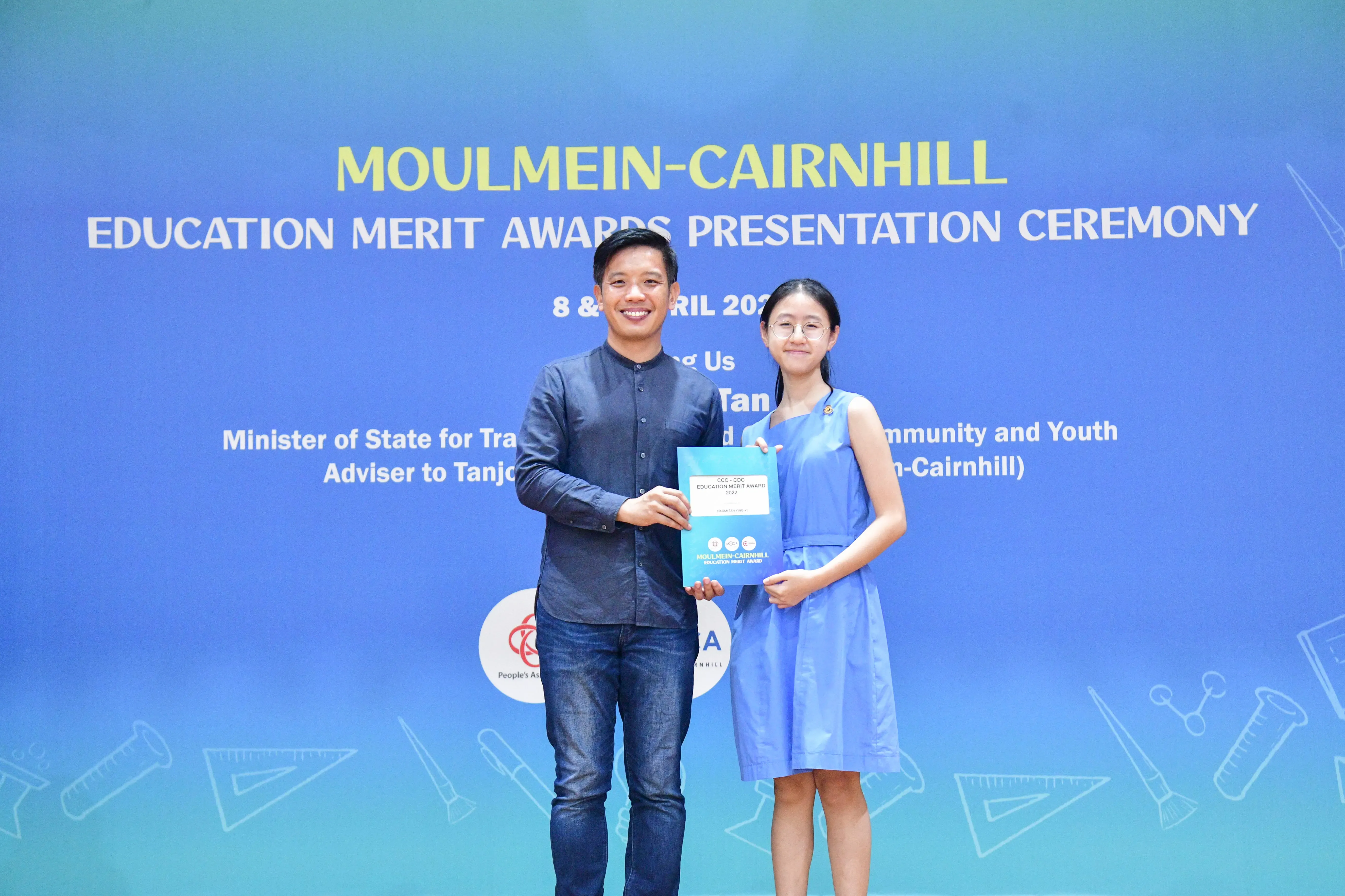 A man and a young girl hold a certificate together at the Moulmein-Cairnhill Education Merit Awards Presentation Ceremony.
