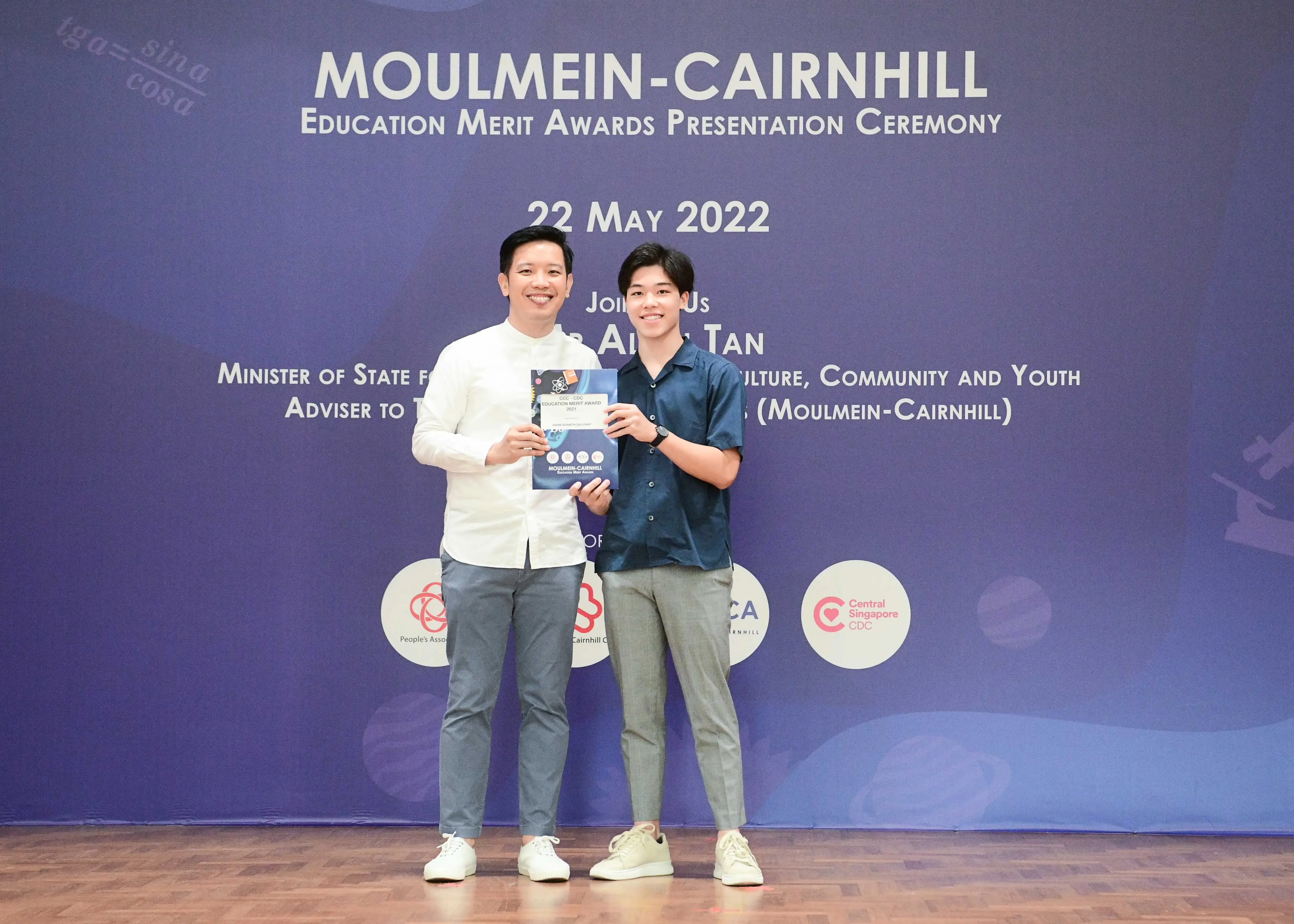 Two men smile holding an award booklet at the Moulmein-Cairnhill Education Merit Awards Ceremony on 22 May 2022.