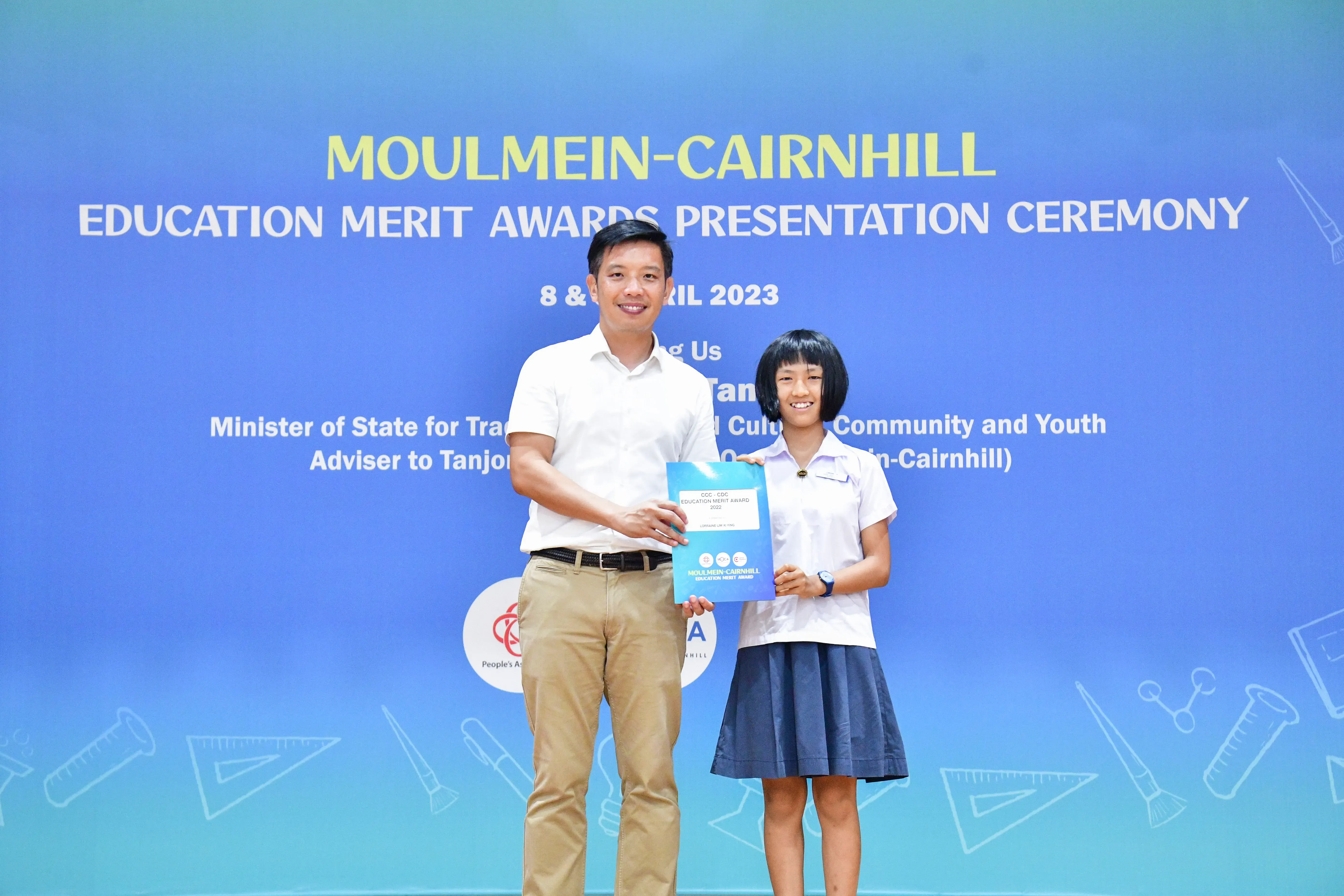 A man and a young girl hold a blue award certificate at the Moulmein-Cairnhill Education Merit Awards 2023.