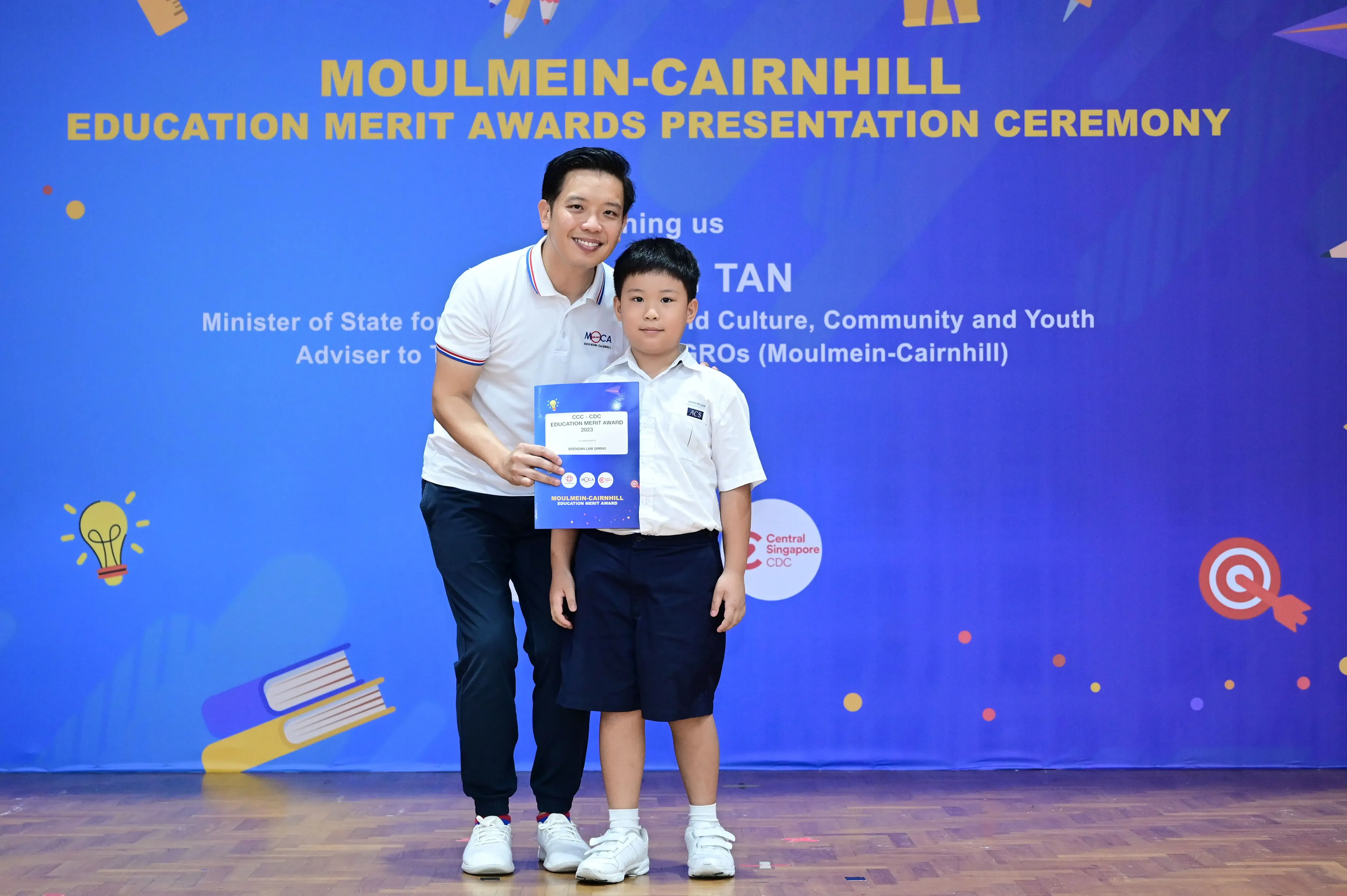 Adult and young boy pose together holding a certificate at Moulmein-Cairnhill Education Merit Awards Ceremony.