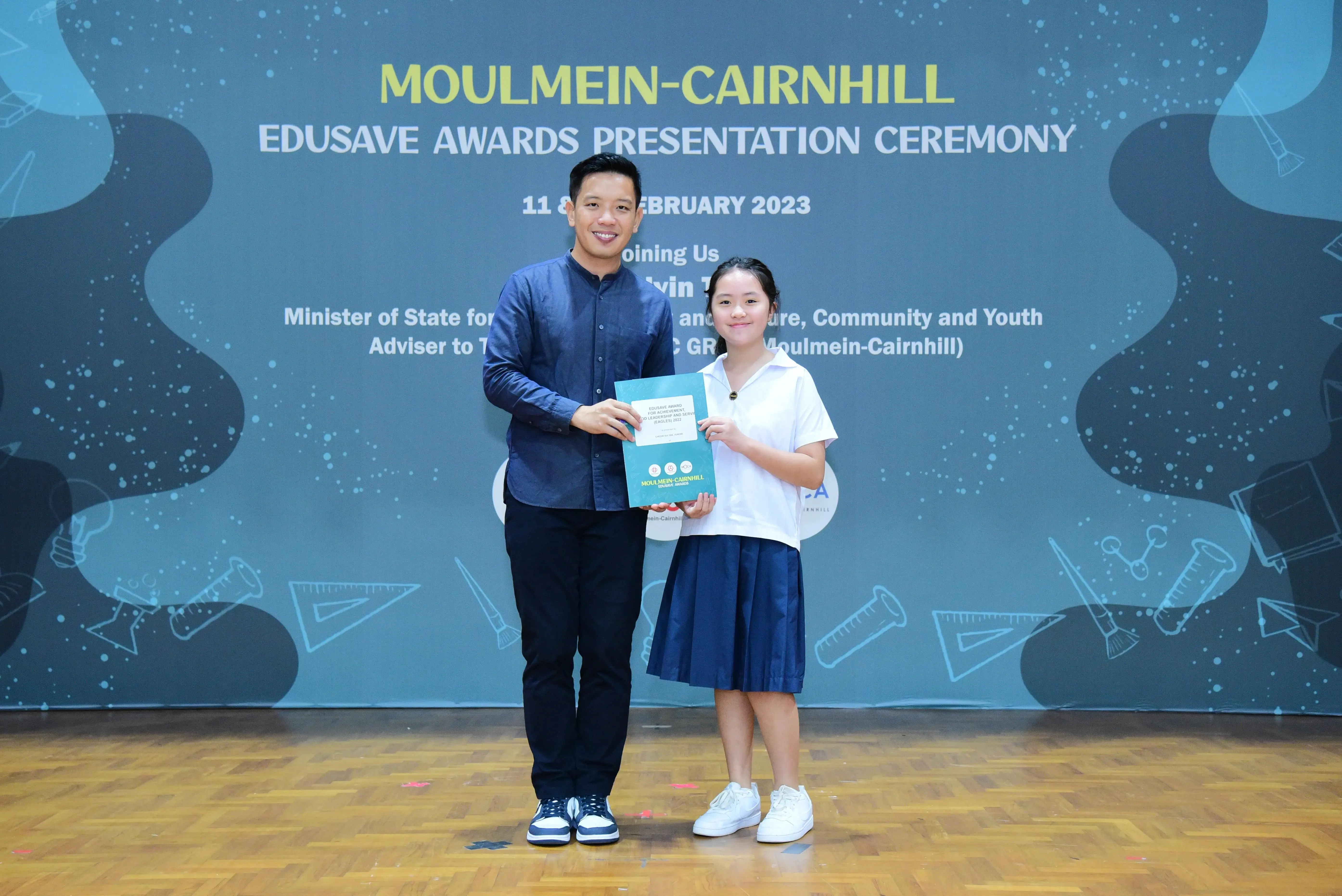 A man and a young girl hold a certificate together at the Moulmein-Cairnhill Edusave Awards Ceremony, February 2023.