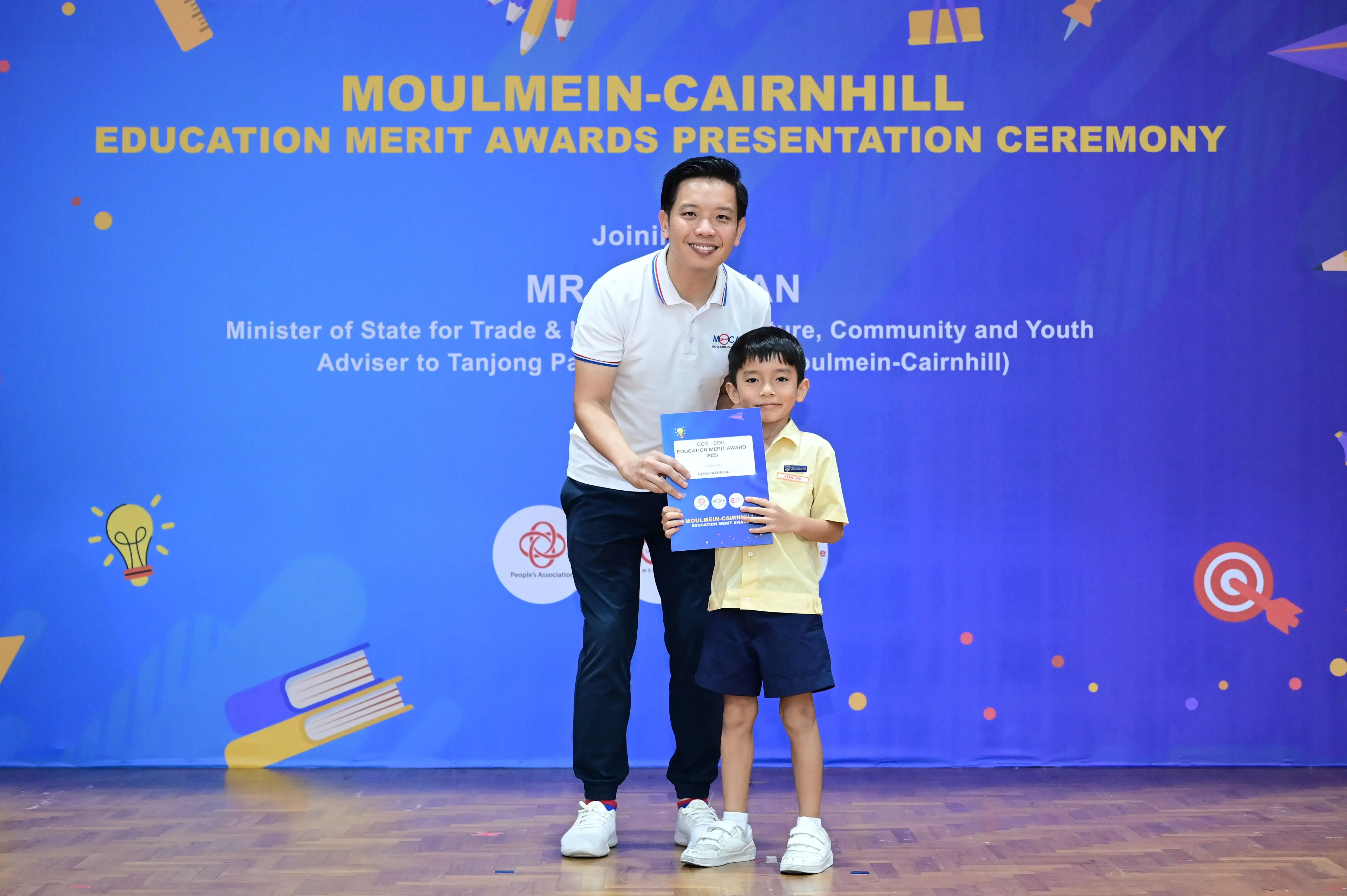 A man and a young boy hold a certificate at the Moulmein-Cairnhill Education Merit Awards Presentation Ceremony.