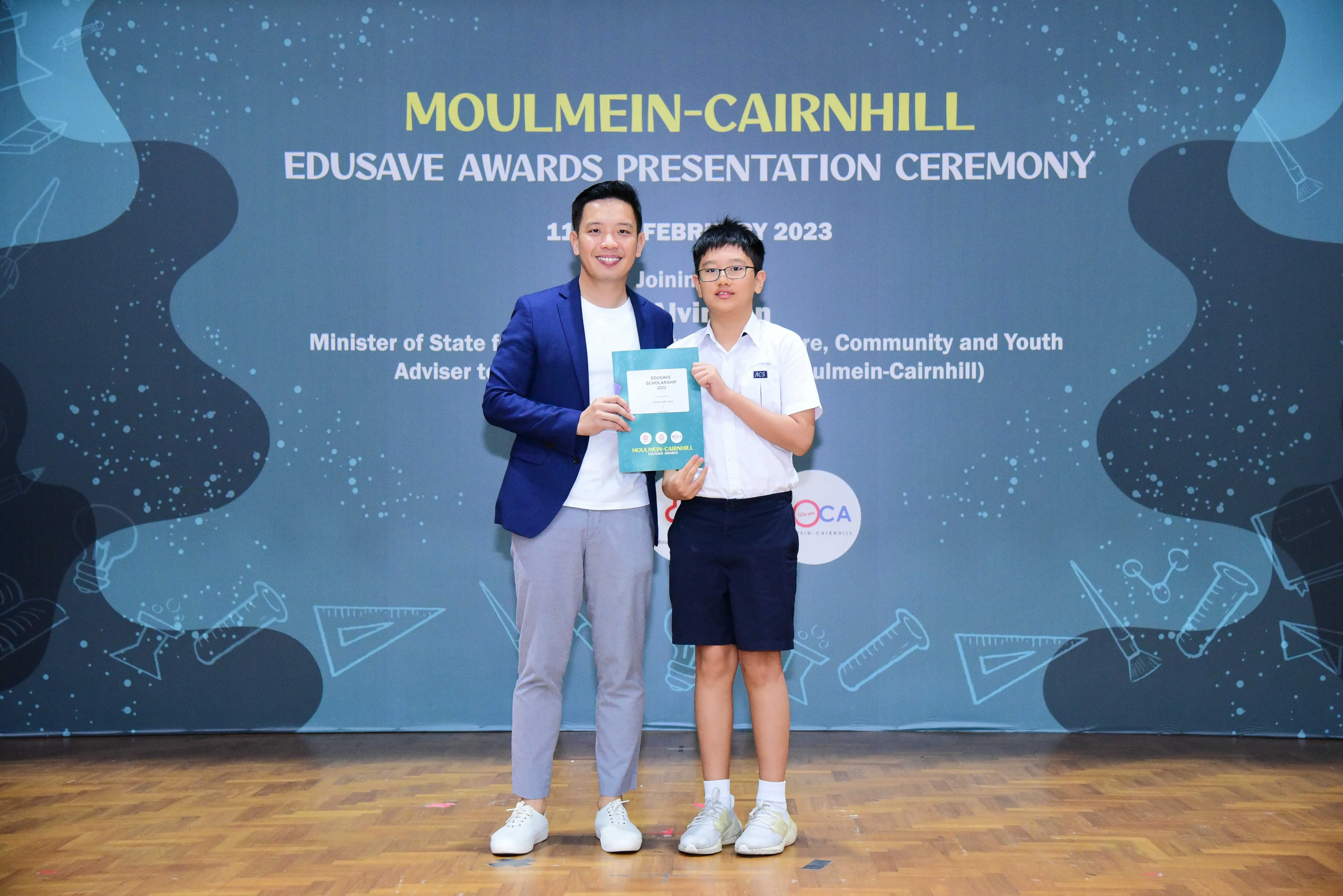 An adult and a young student hold a certificate at the Moulmein-Cairnhill Edusave Awards Ceremony, February 2023.