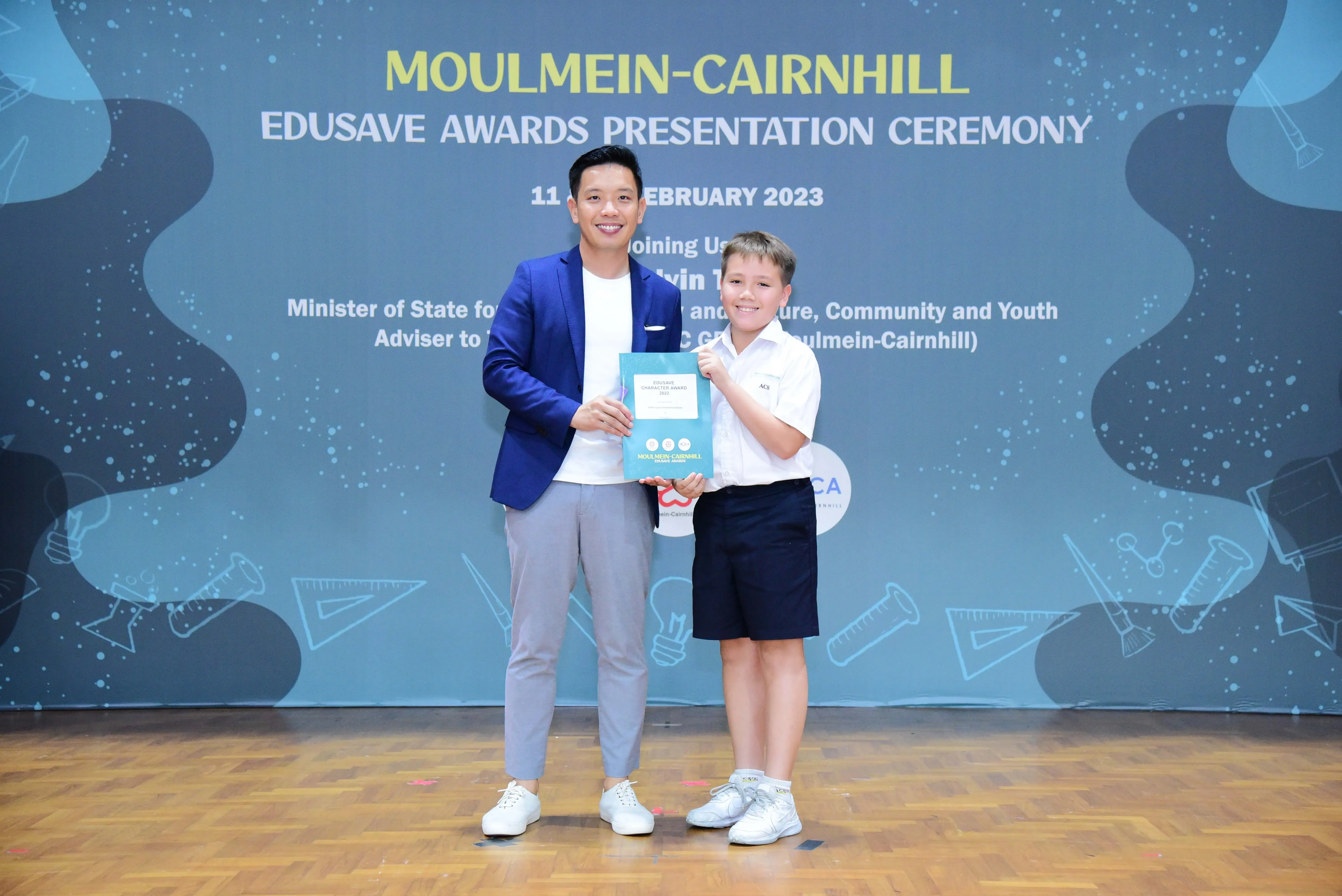A man in a blue blazer and a young boy in school uniform hold a certificate at the Moulmein-Cairnhill Edusave Awards 2023.