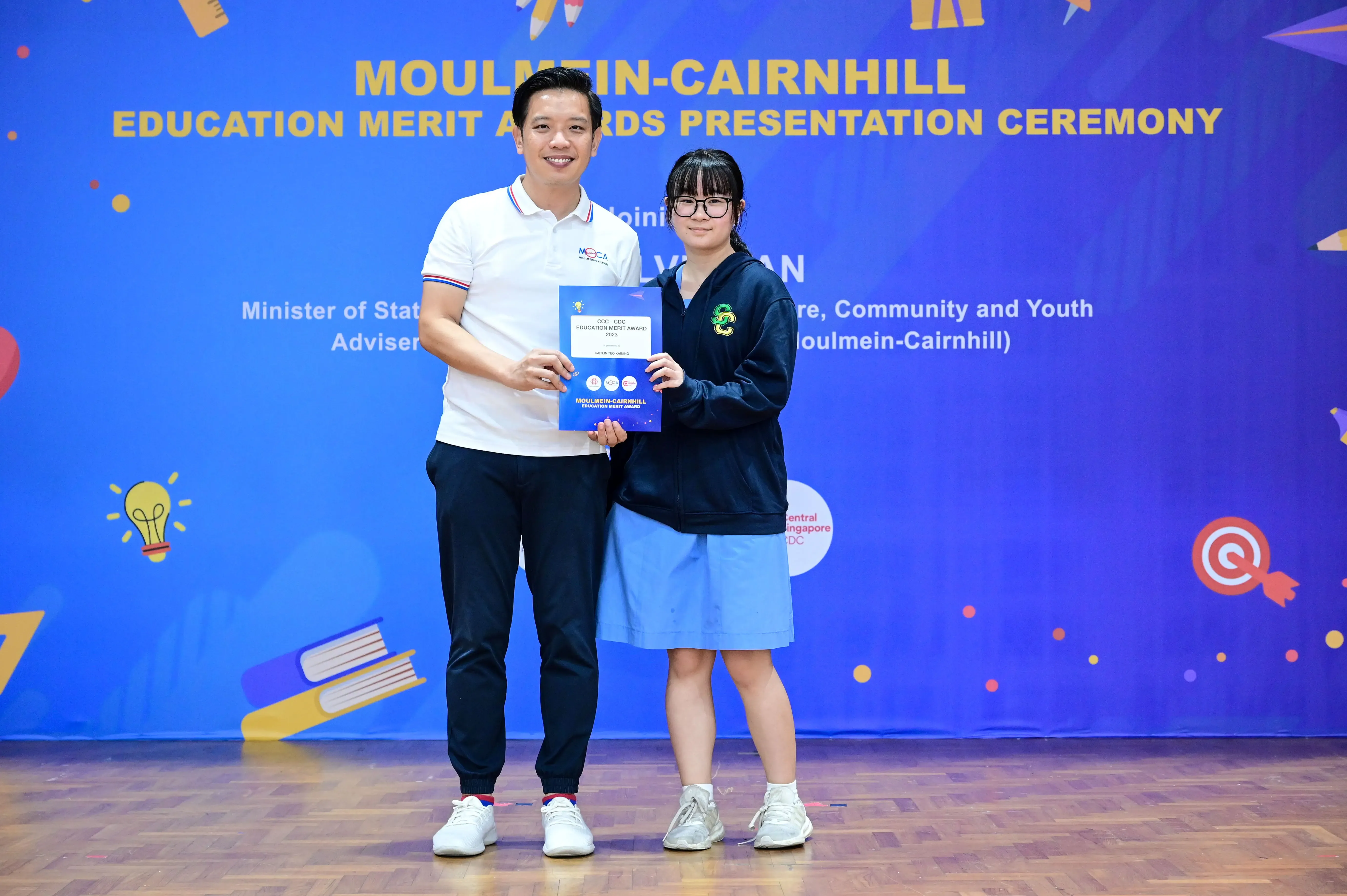 A man and a girl hold a certificate together at the Moulmein-Cairnhill Education Merit Awards Presentation Ceremony.
