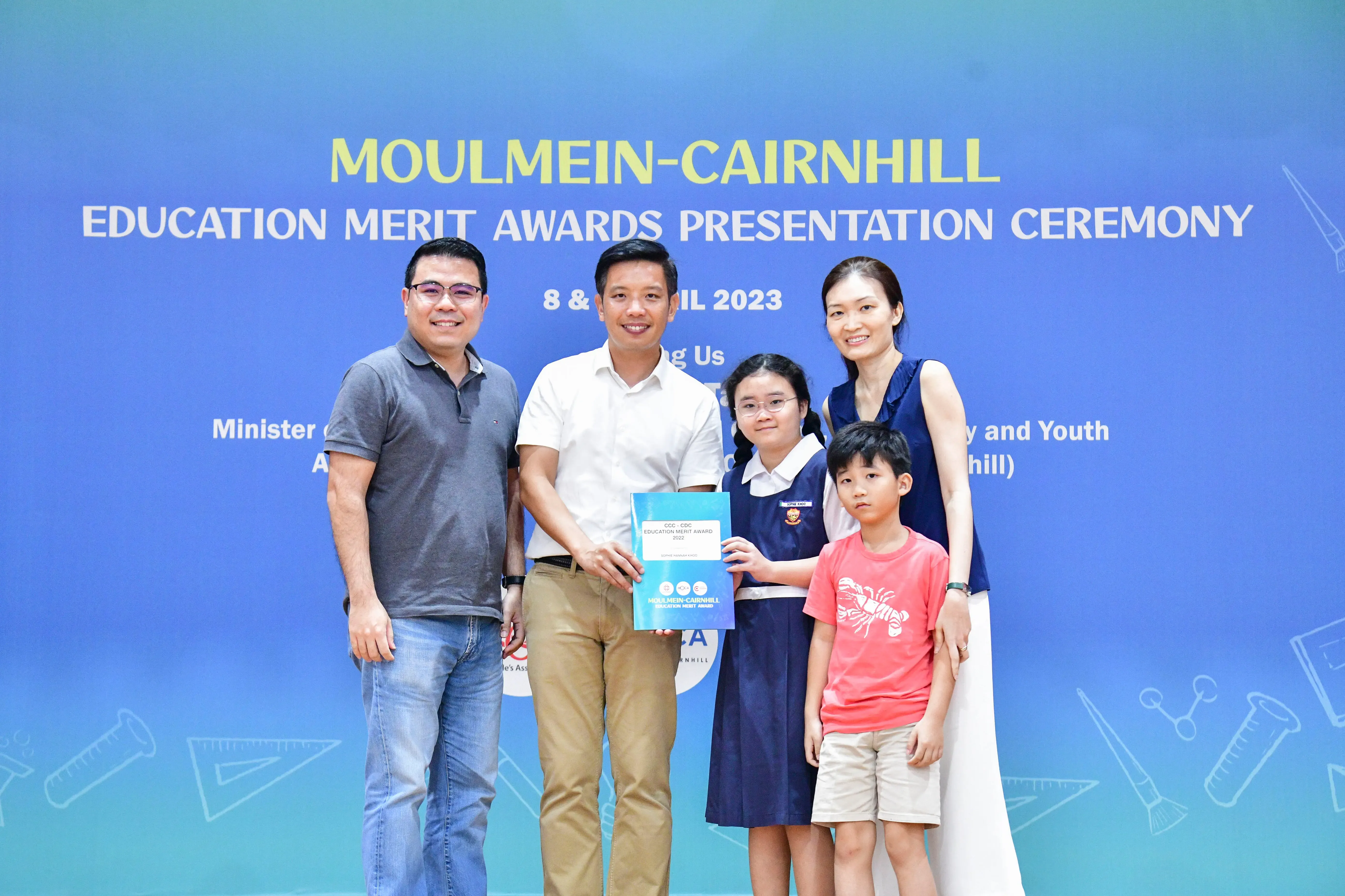Five people pose before a Moulmein-Cairnhill Education Merit Awards Presentation Ceremony 2023 banner.