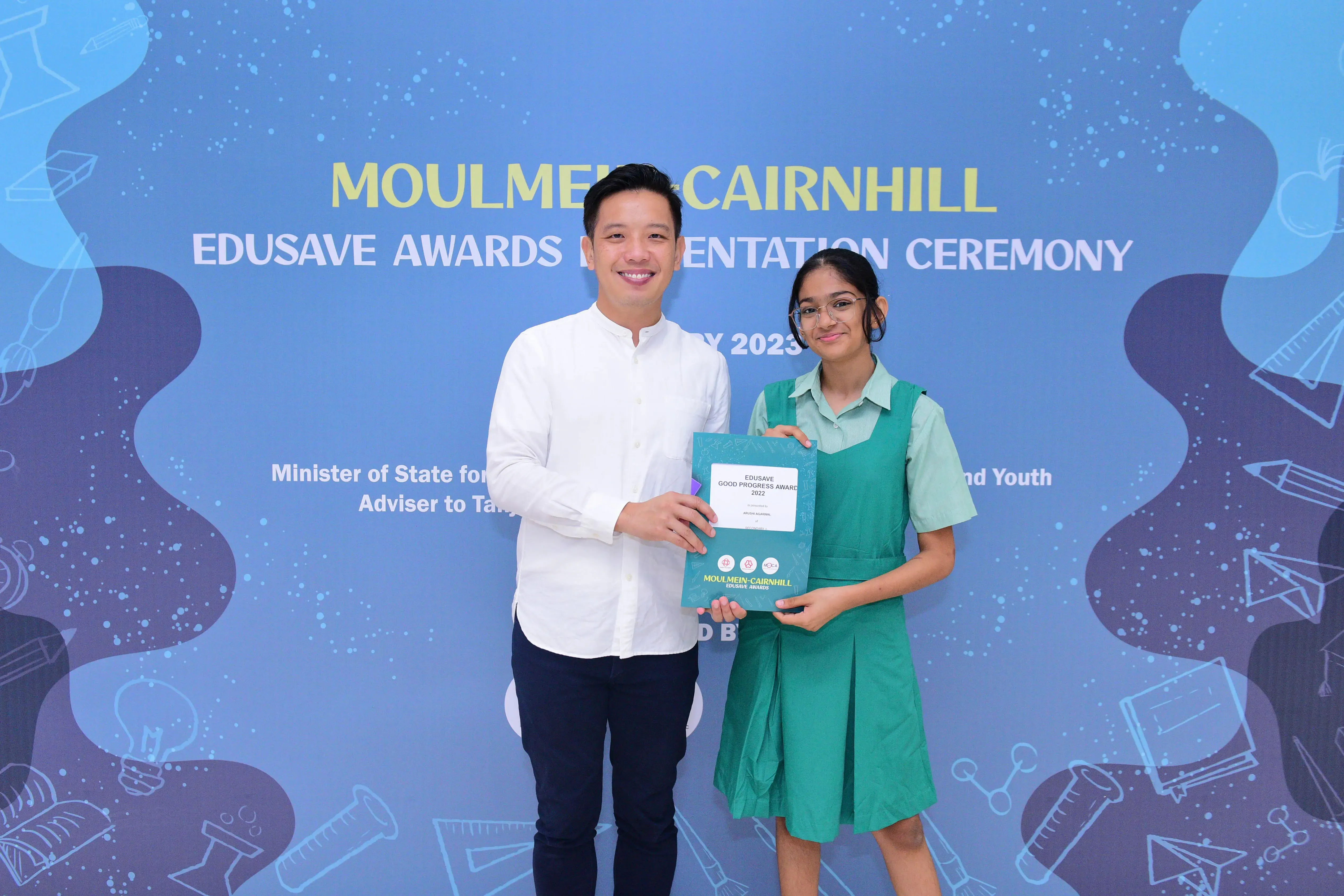 A man and a girl hold an Edusave Good Progress Award certificate at the Moulmein-Cairnhill Awards Ceremony 2023.