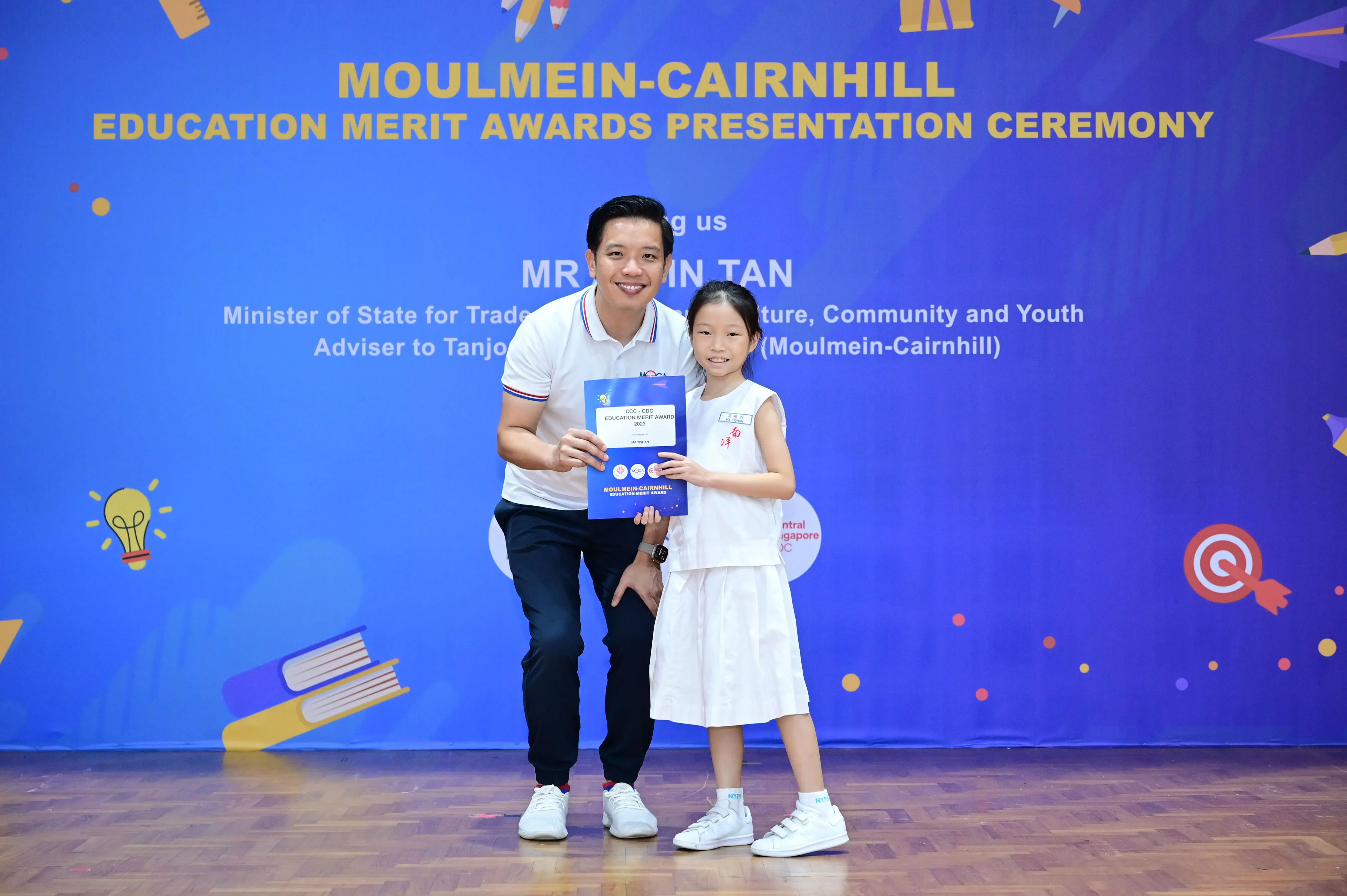 A man and a young girl hold a certificate together at the Moulmein-Cairnhill Education Merit Awards Presentation Ceremony.