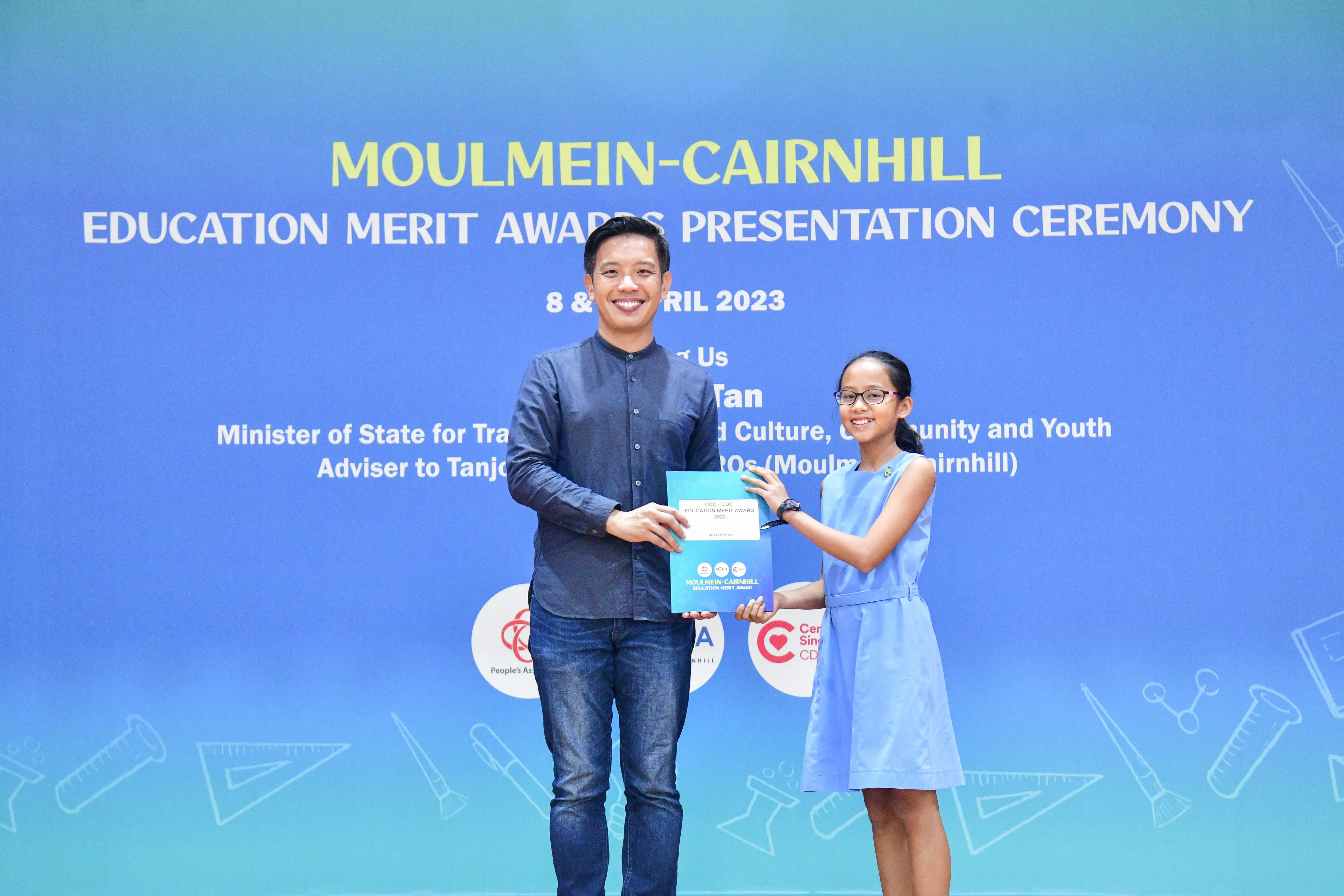 A man and a young girl hold a certificate together at the Moulmein-Cairnhill Education Merit Awards Ceremony, April 2023.