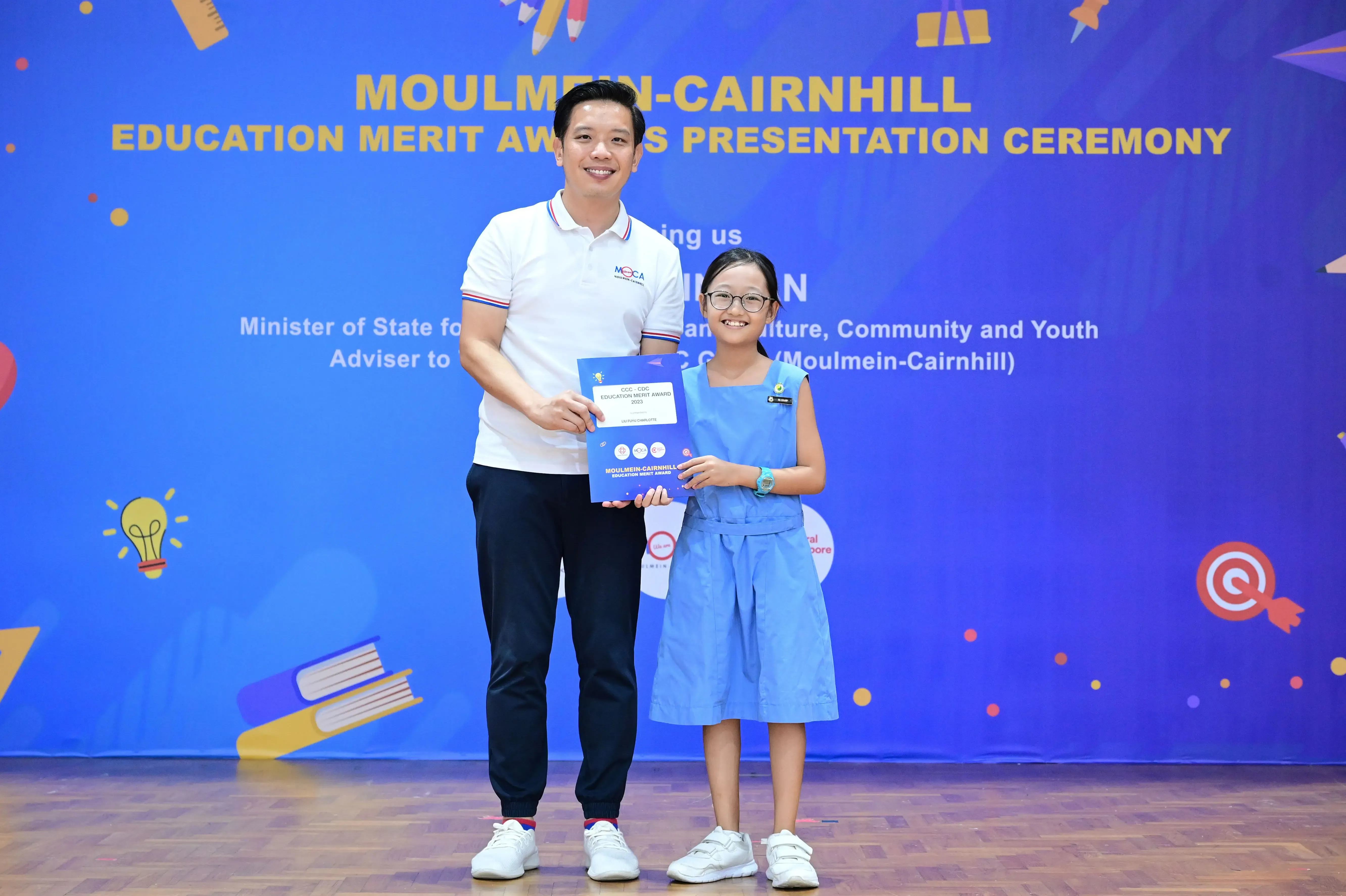 Man and young girl hold a certificate at the Moulmein-Cairnhill Education Merit Awards Presentation Ceremony.
