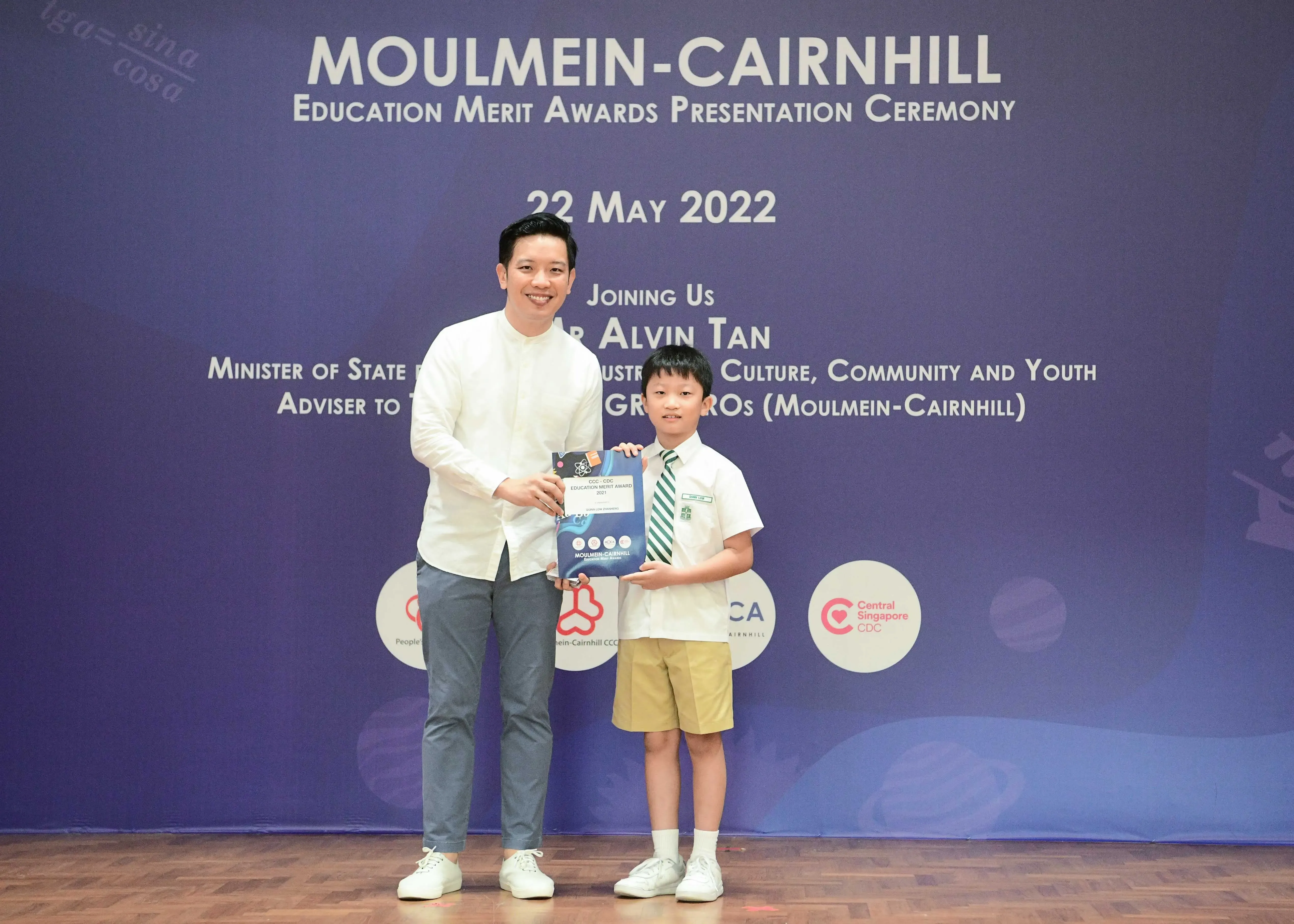 A man and a young boy hold an award together on stage at the Moulmein-Cairnhill Education Merit Awards on 22 May 2022.