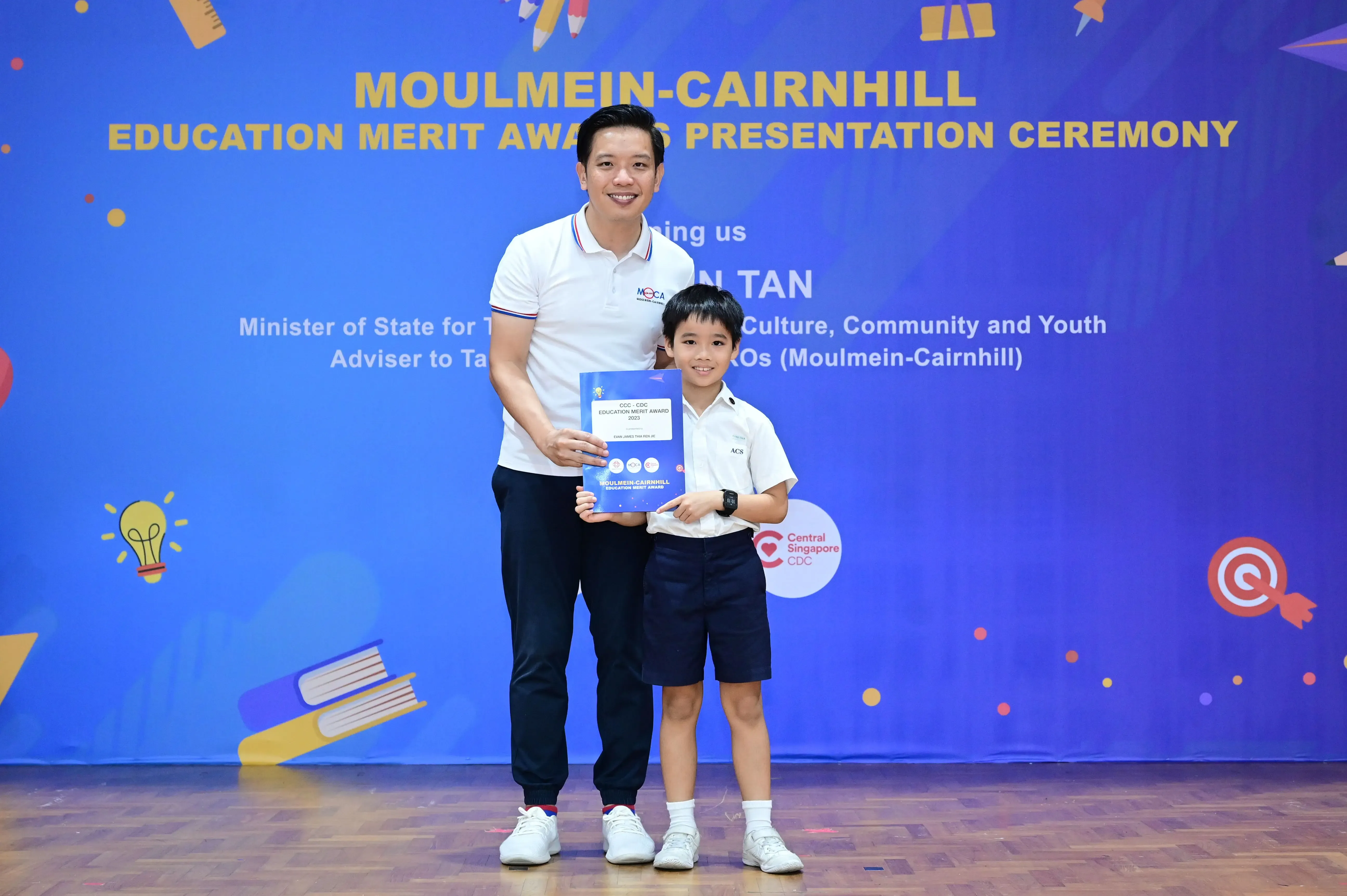 Man and young boy holding a certificate at the Moulmein-Cairnhill Education Merit Award Presentation Ceremony.