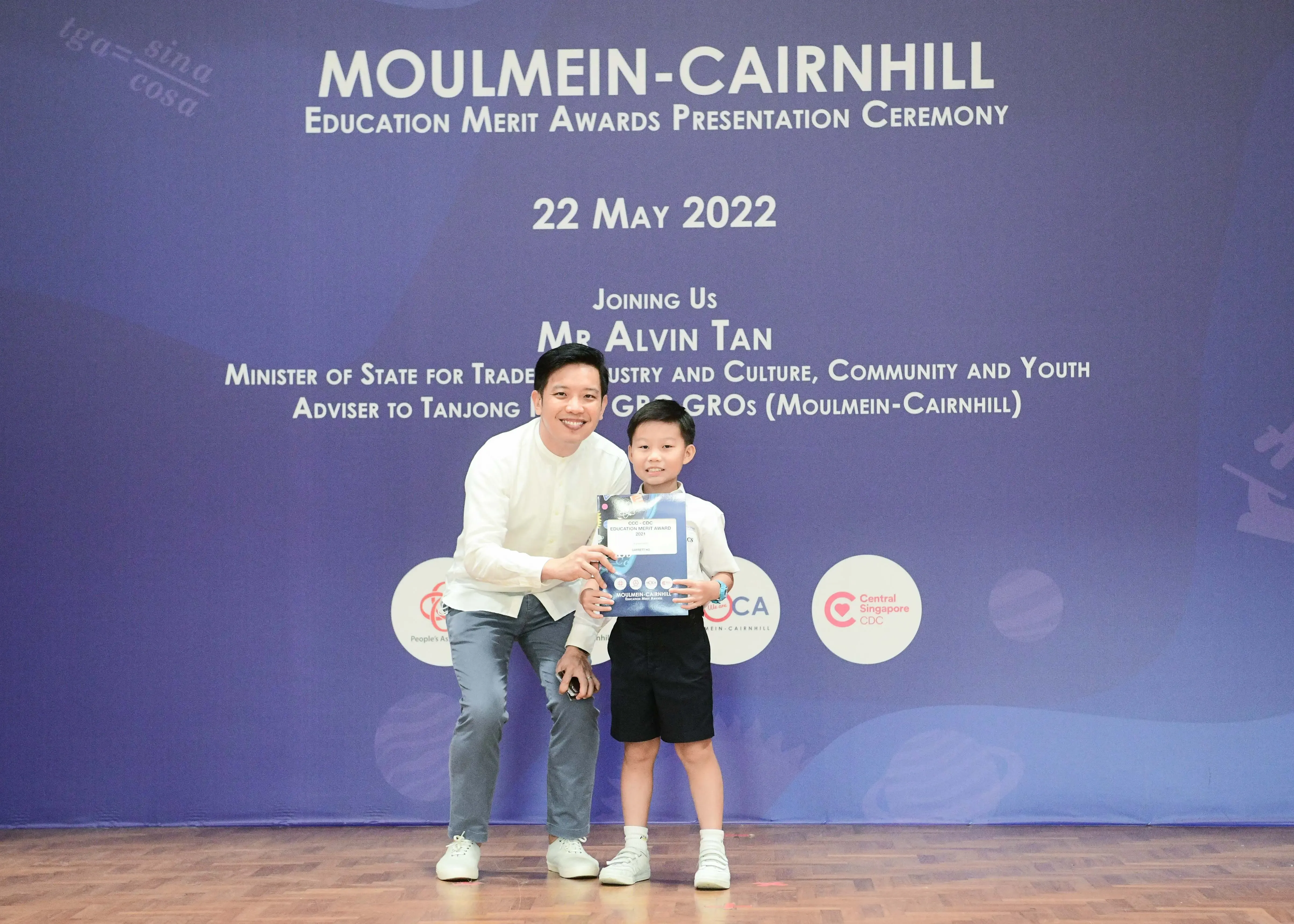 A man and a young boy hold a certificate at the Moulmein-Cairnhill Education Merit Awards ceremony on 22 May 2022.