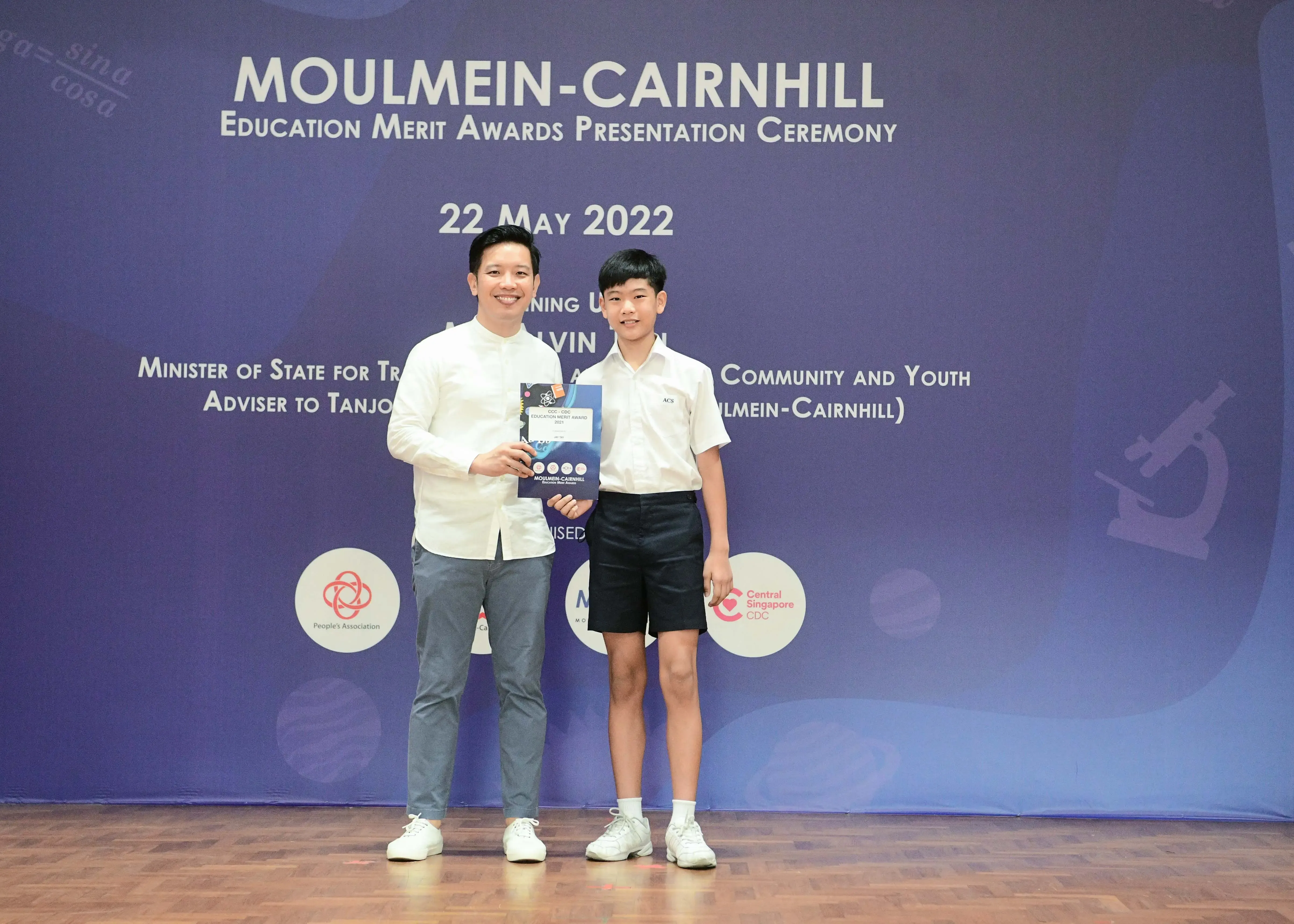 An adult man and a young boy pose together at the Moulmein-Cairnhill Education Merit Awards Ceremony on 22 May 2022.