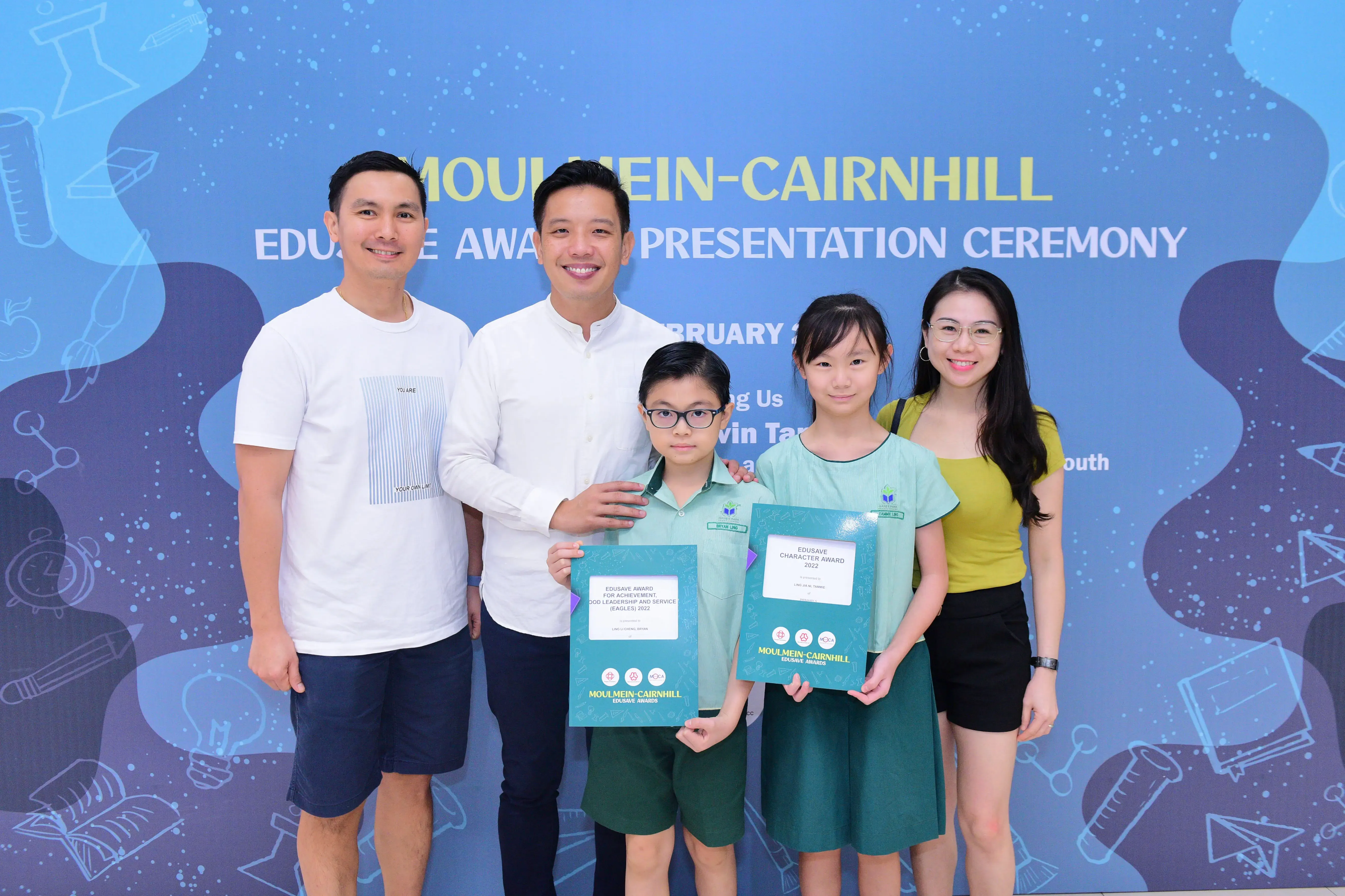 Two children holding Edusave award certificates pose with three adults at the Moulmein-Cairnhill Edusave Award Ceremony.