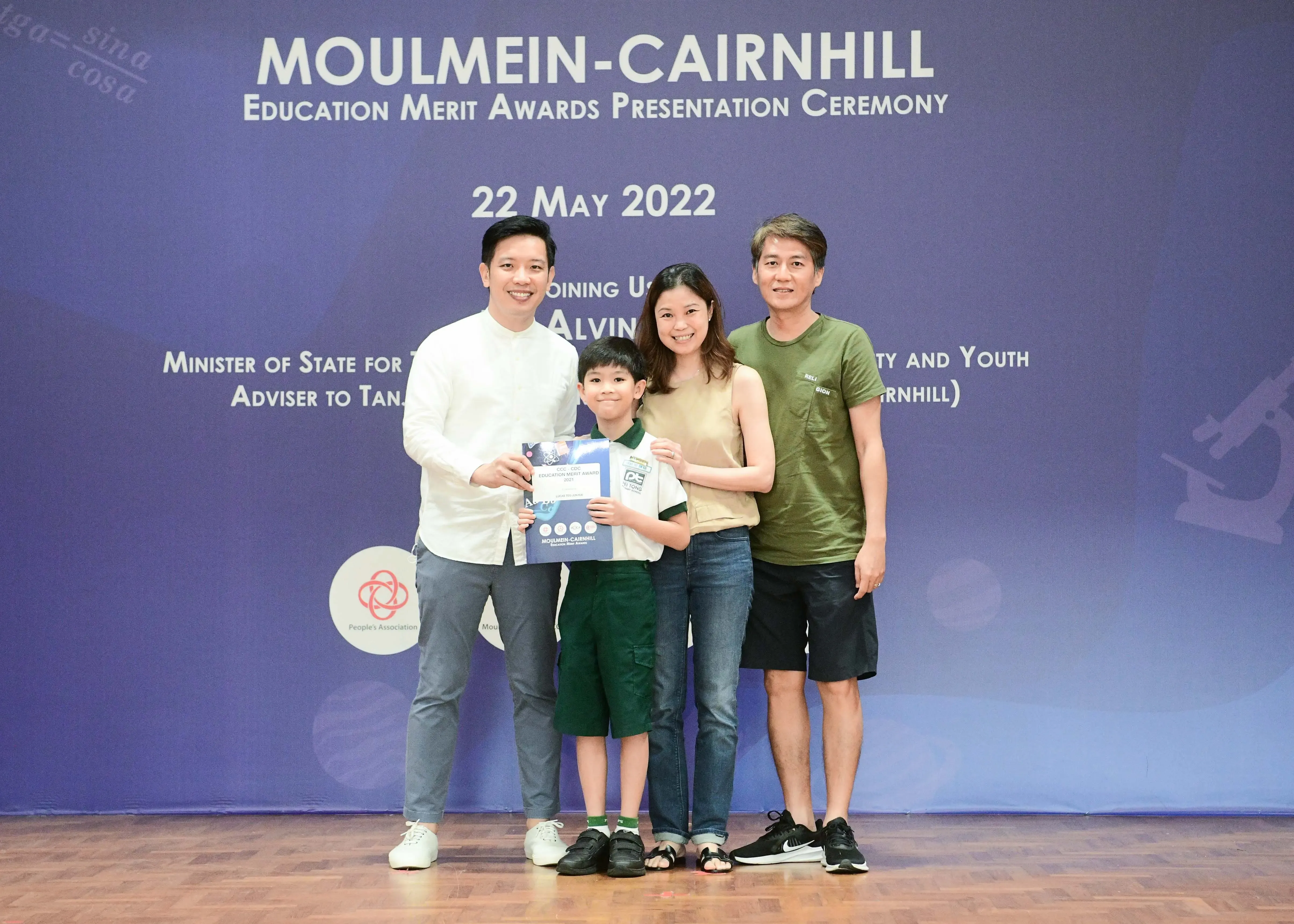 Four people pose on a stage at the Moulmein-Cairnhill Education Merit Awards ceremony on 22 May 2022, holding a certificate.