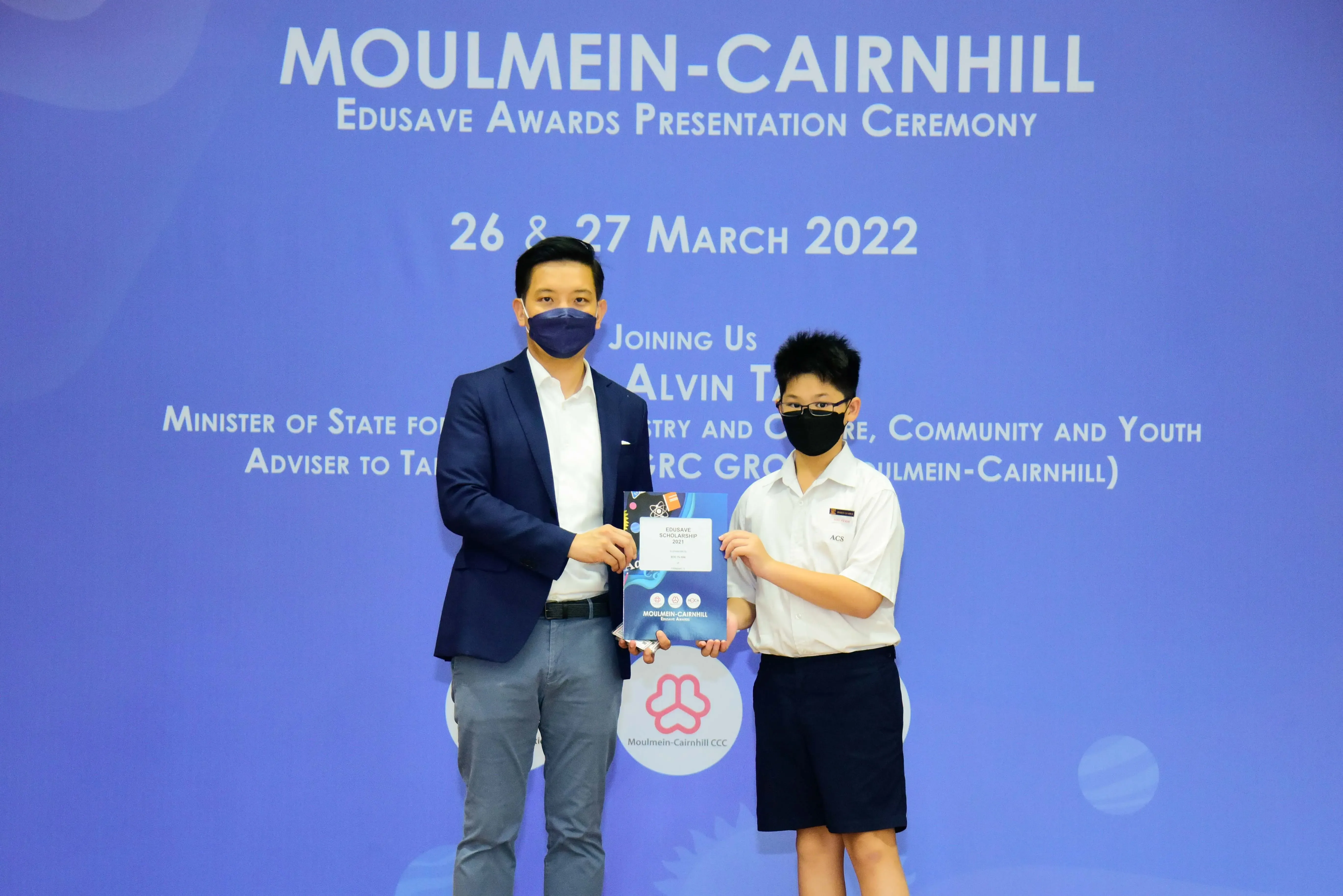 Two masked individuals hold an award at the Moulmein-Cairnhill Edusave Awards Presentation Ceremony, March 2022.