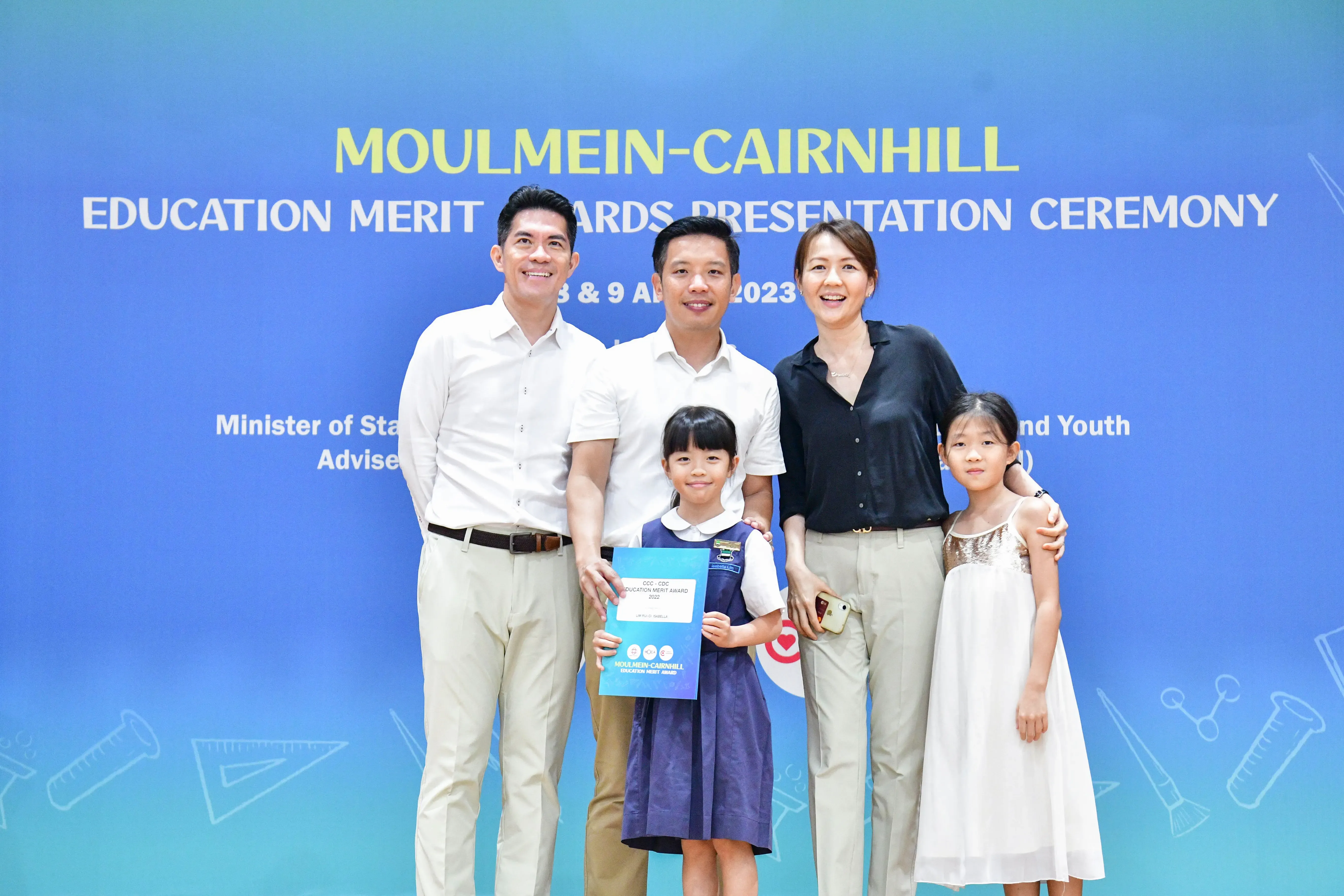 Five people pose at the Moulmein-Cairnhill Education Merit Awards Presentation Ceremony 2023, with a girl holding a certificate.