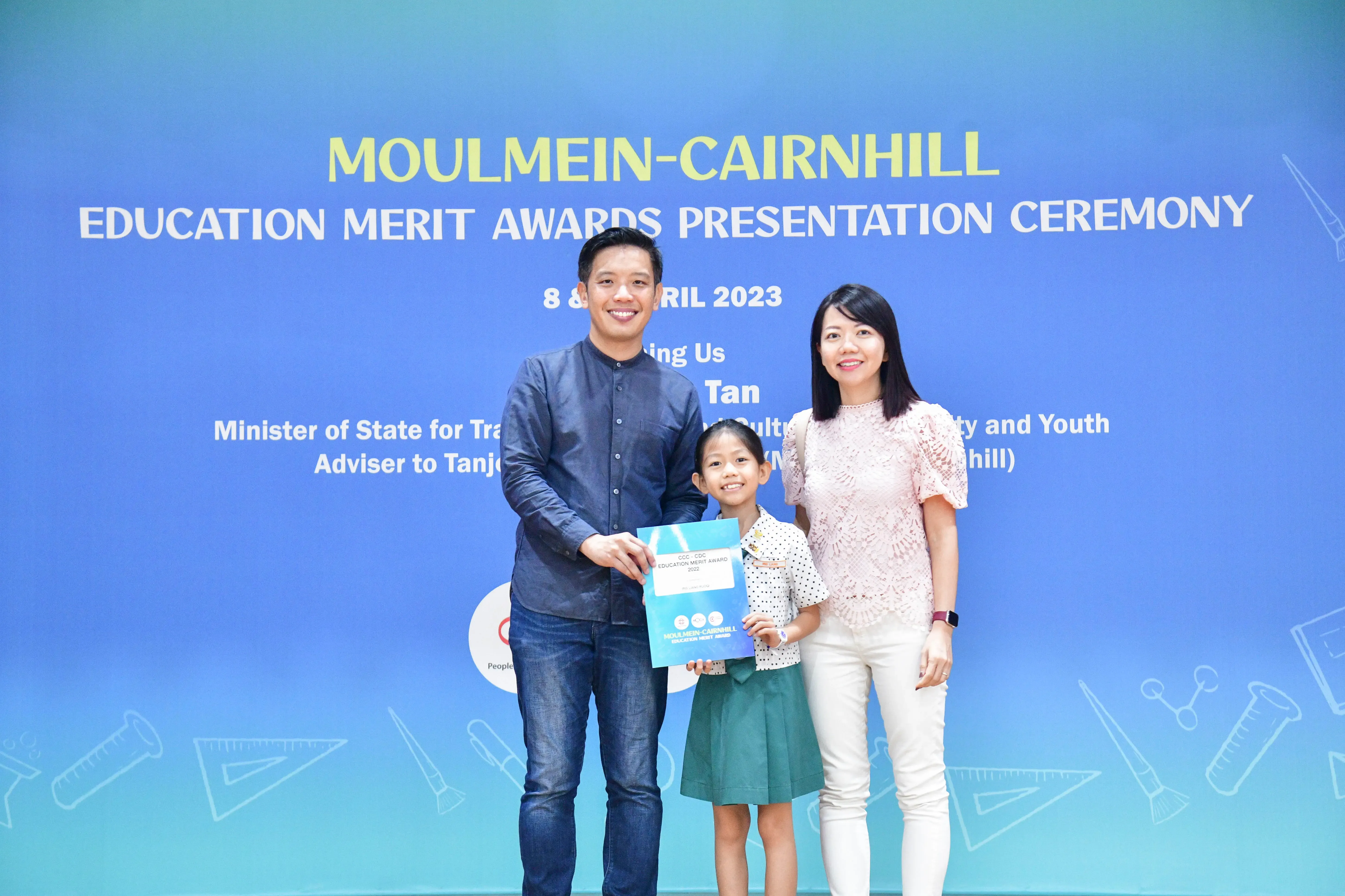 A man and woman pose with a young girl holding an award at the Moulmein-Cairnhill Education Merit Awards Ceremony 2023.