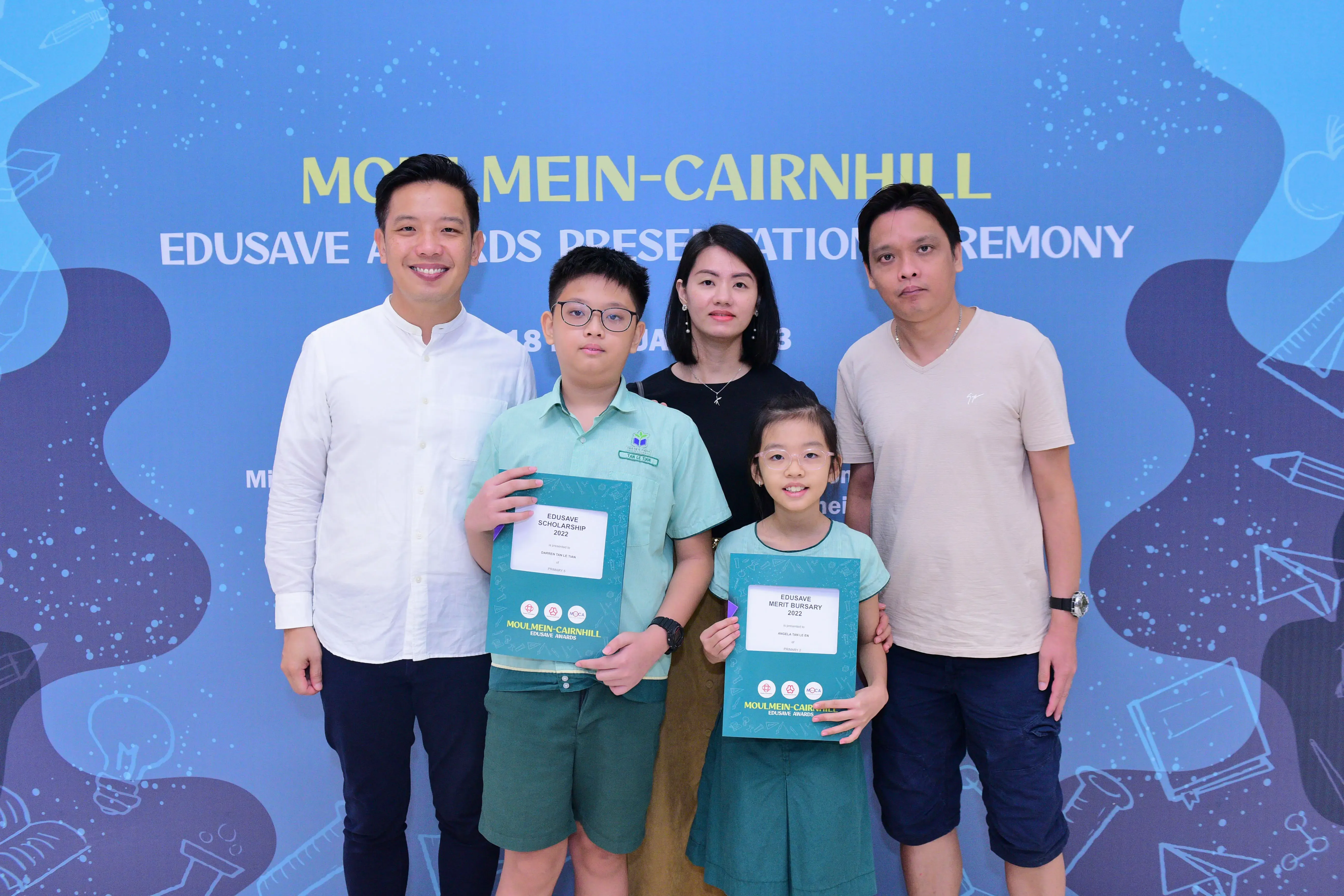 Two children holding Edusave award certificates pose with three adults at the Moulmein-Cairnhill Edusave Awards Ceremony.
