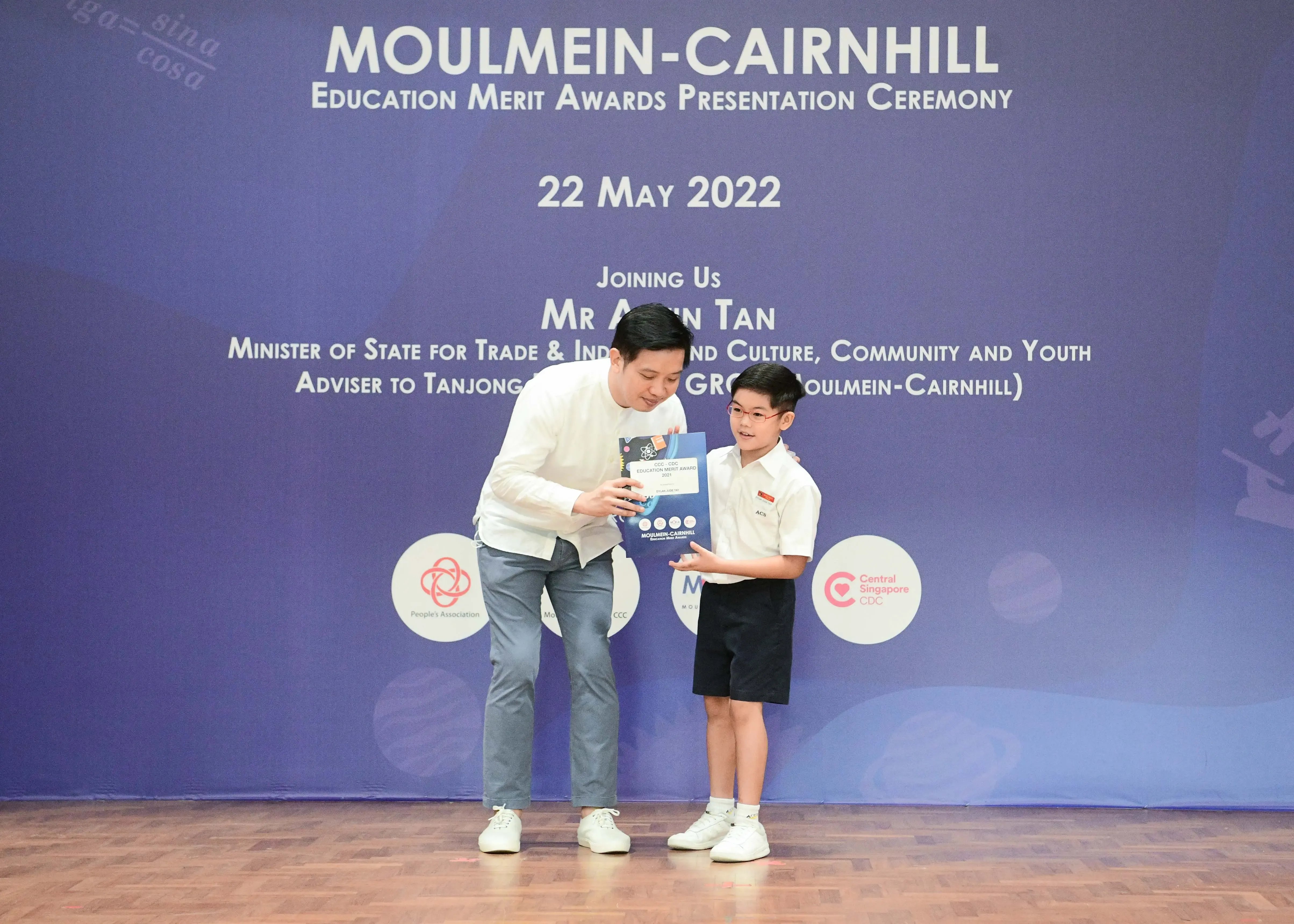 An adult man presents a certificate to a young boy at the Moulmein-Cairnhill Education Merit Awards on 22 May 2022.