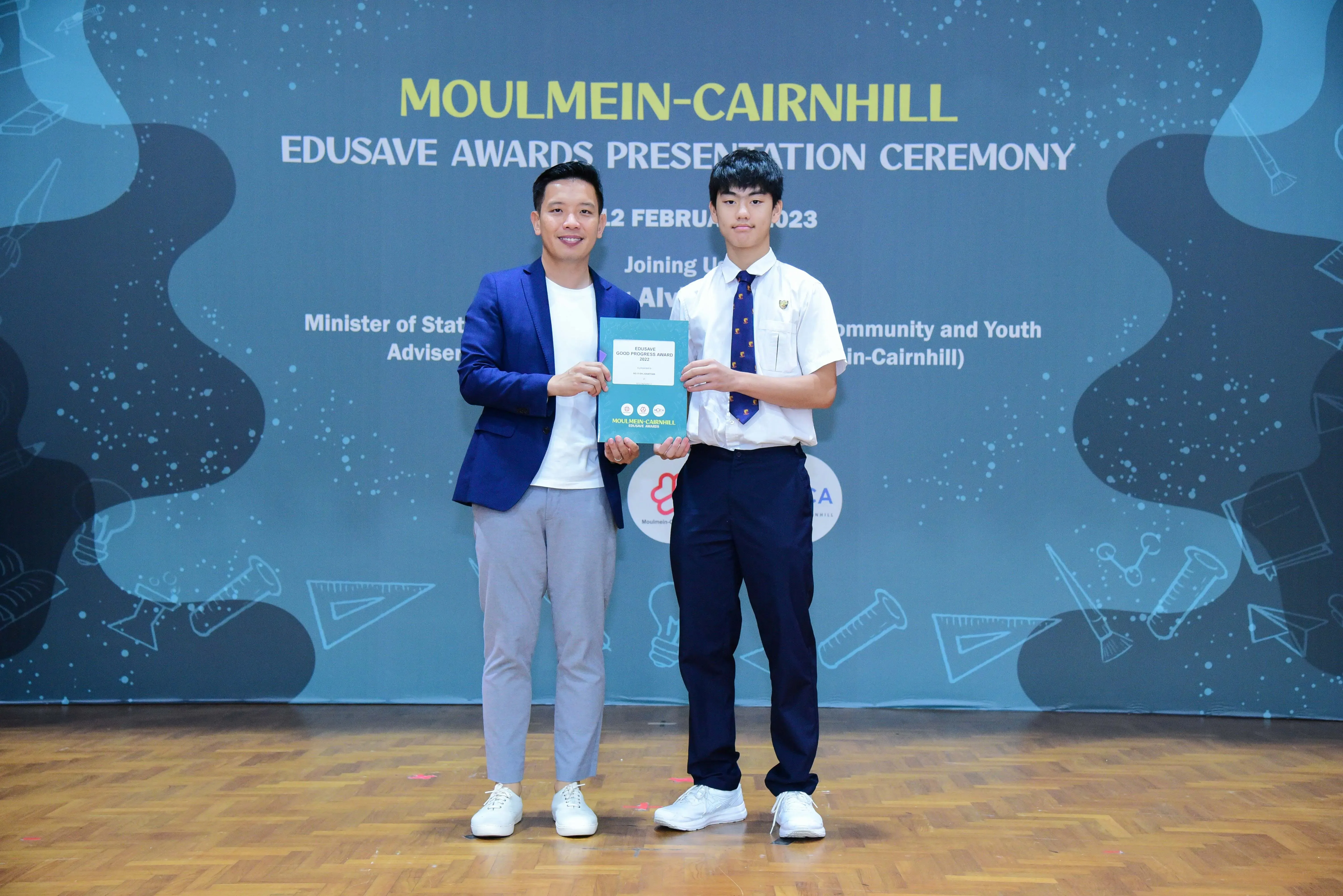 Two men pose holding an award booklet at the Moulmein-Cairnhill Edusave Awards Presentation Ceremony 2023.