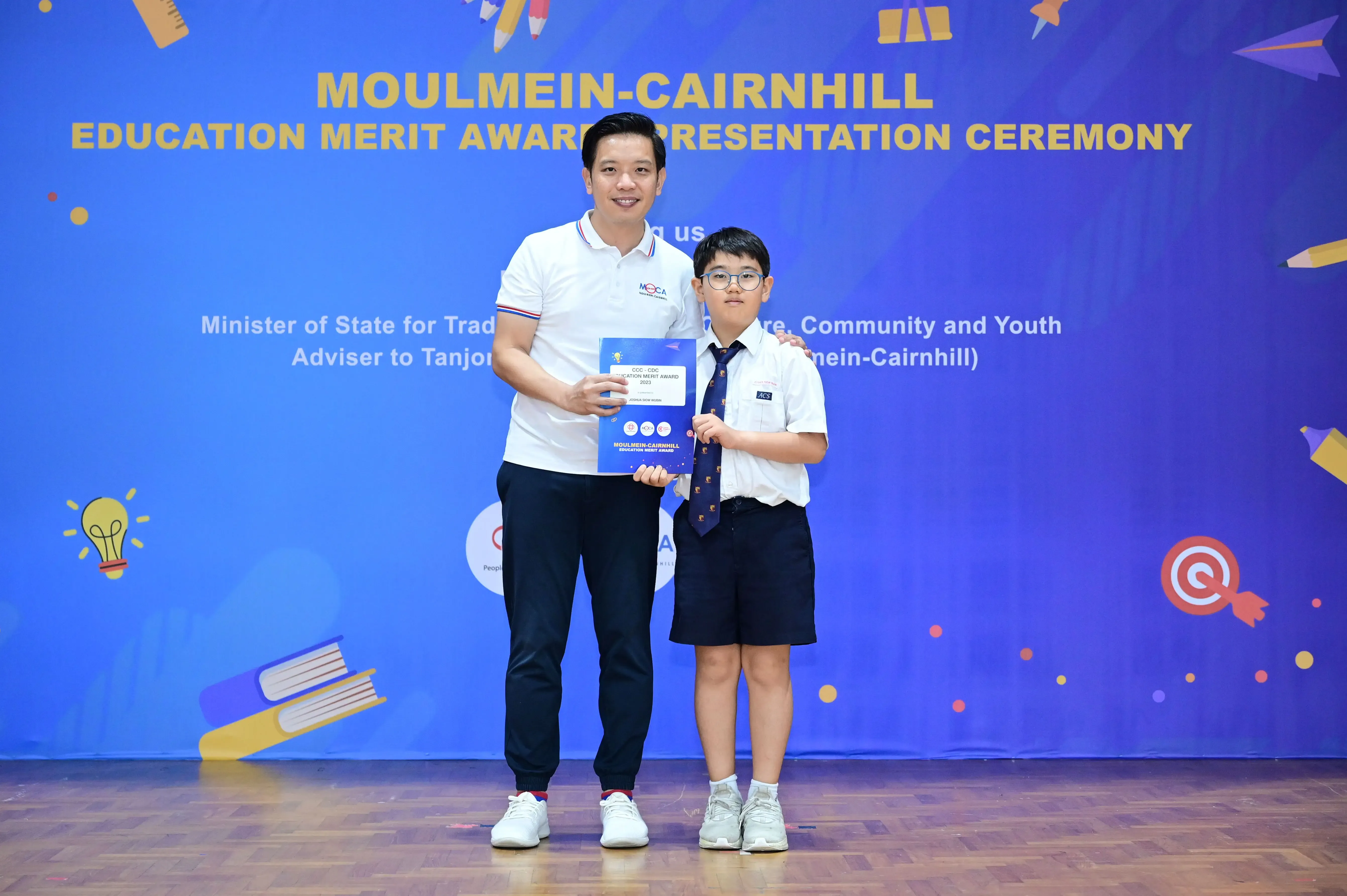 Adult and young boy holding a certificate at Moulmein-Cairnhill Education Merit Award Presentation Ceremony.