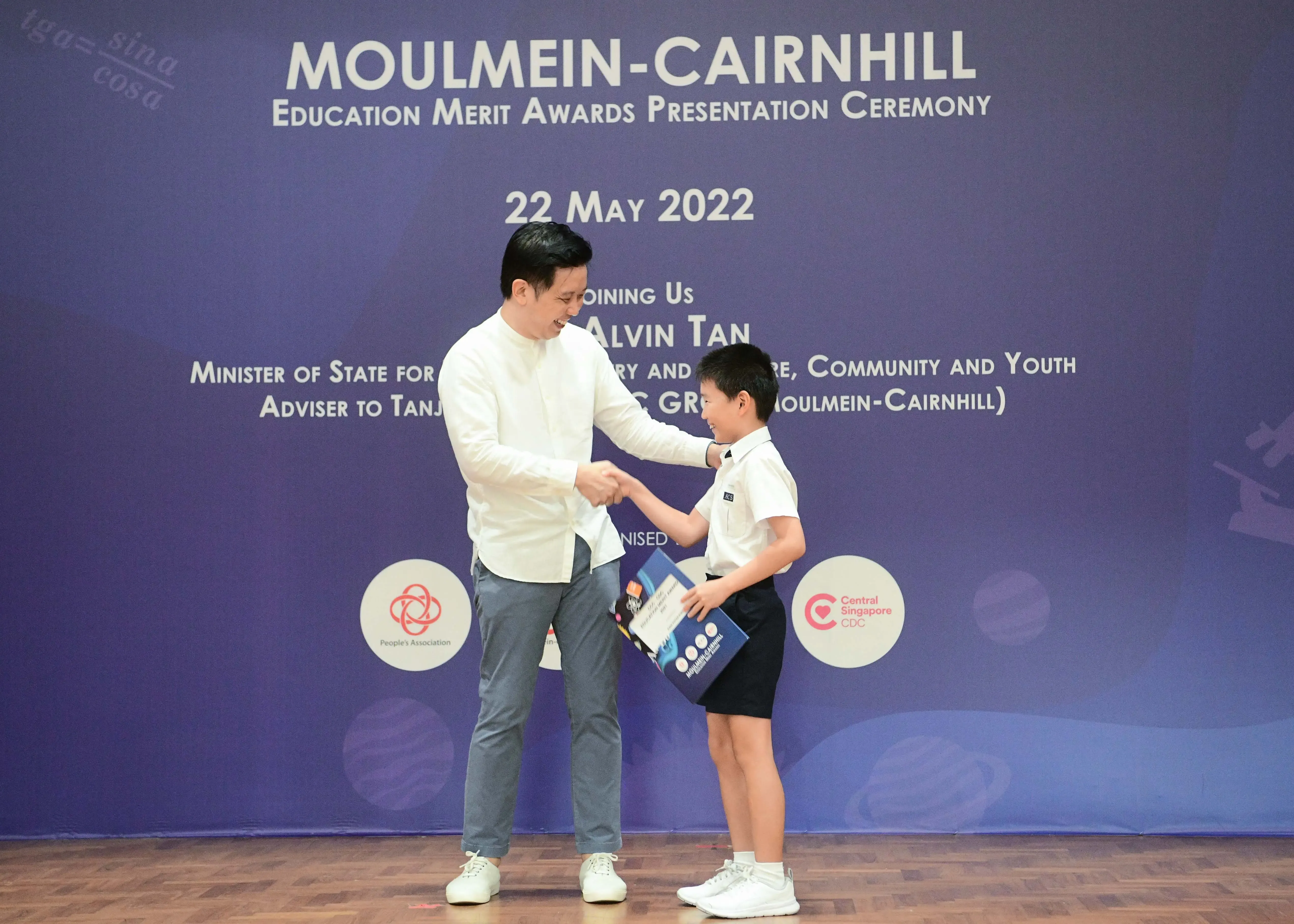 A man shakes hands with a young boy holding an award at the Moulmein-Cairnhill Education Merit Awards Ceremony, 22 May 2022.