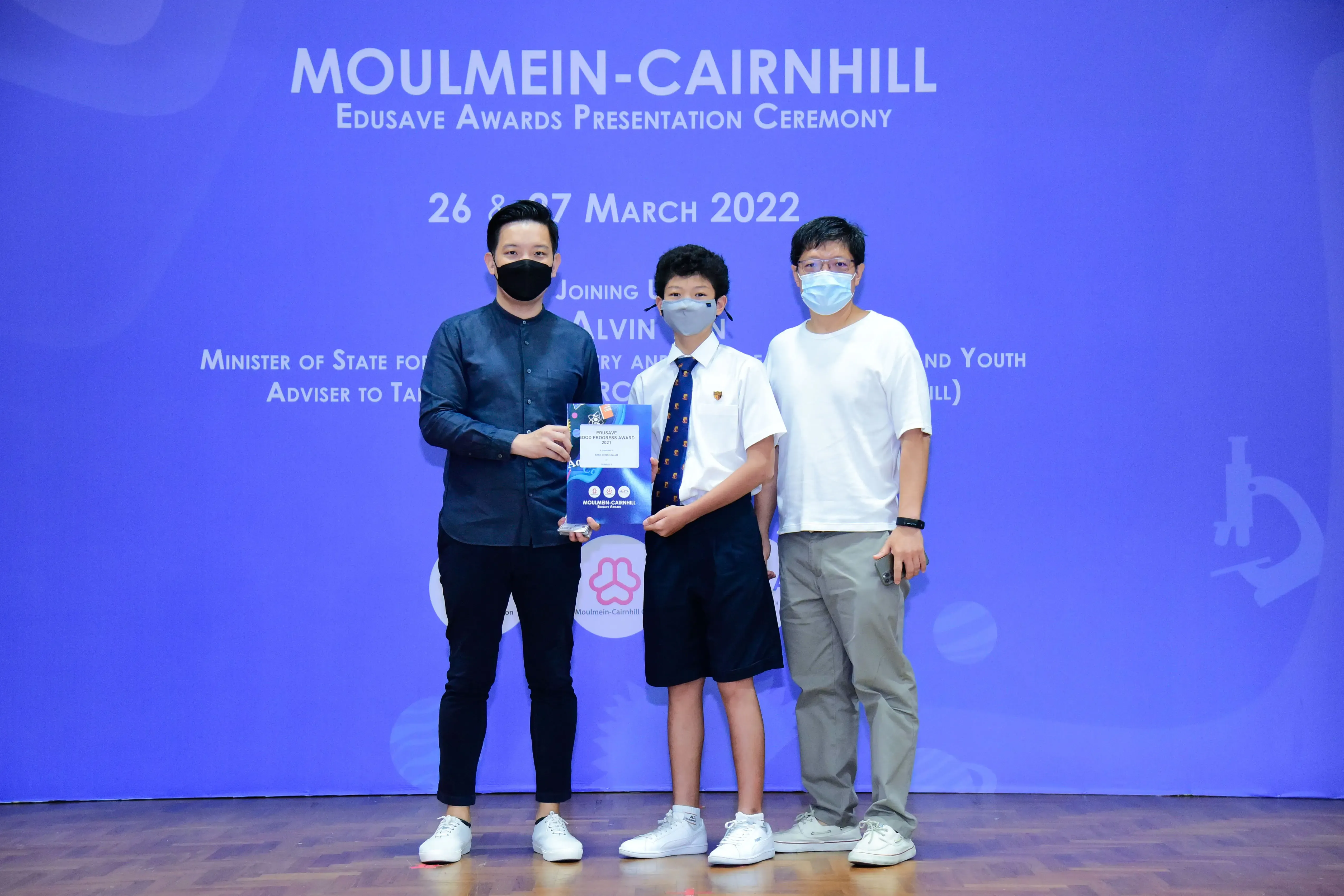 Three masked people pose with an award at the Moulmein-Cairnhill Edusave Awards Ceremony, March 2022.
