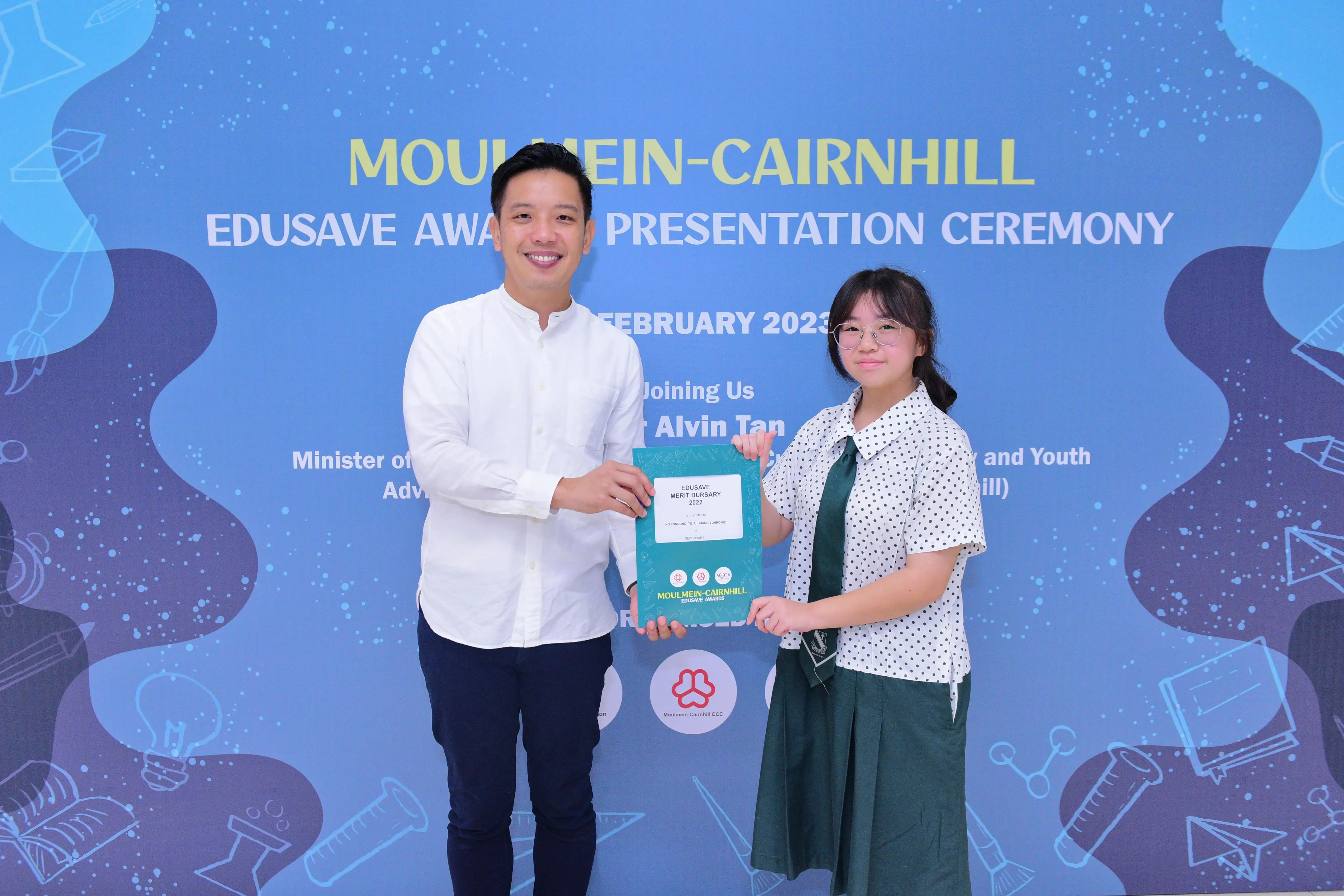 Two people hold an Edusave Merit Bursary certificate at the Moulmein-Cairnhill Edusave Awards Ceremony, February 2023.