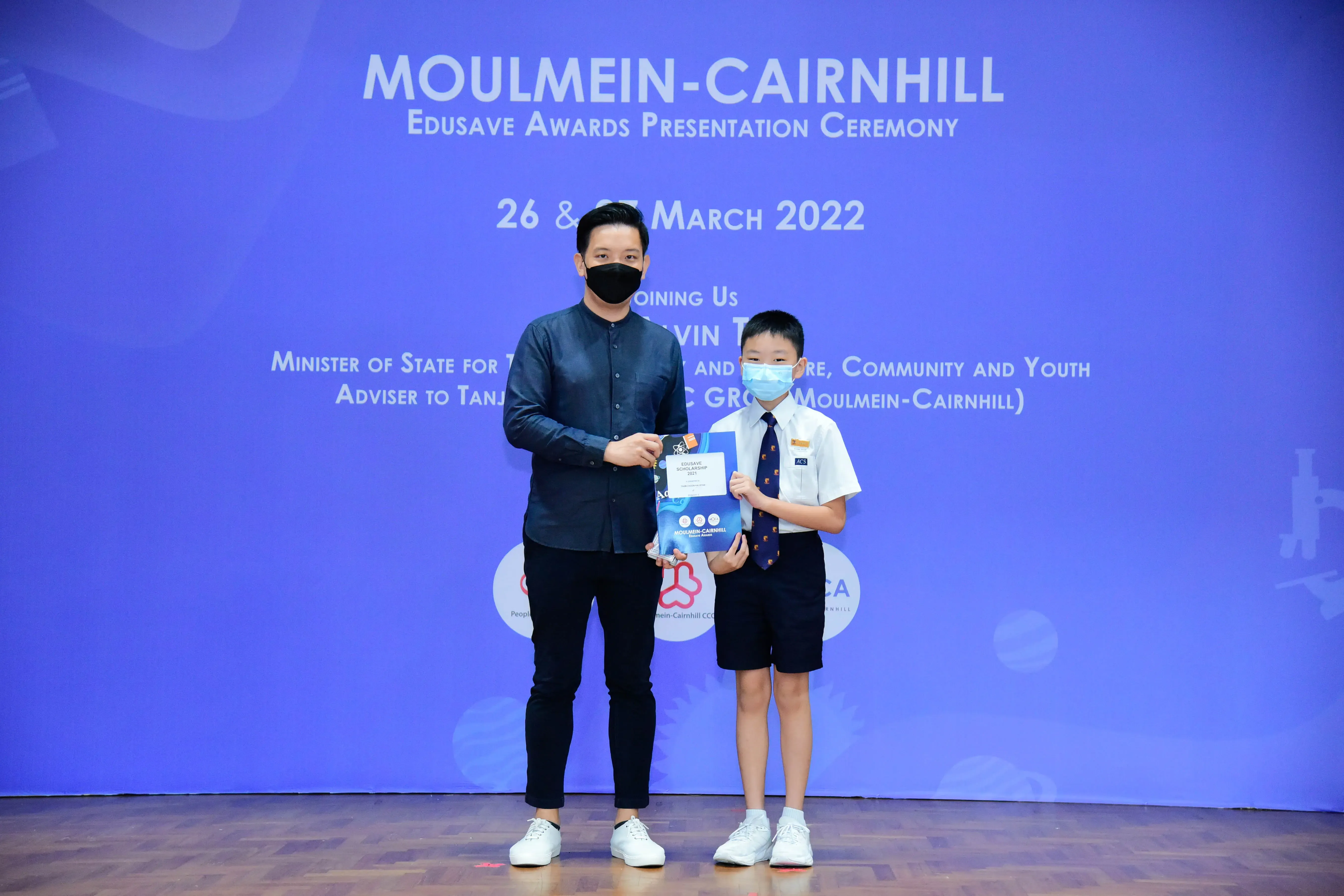 An adult and a young student in uniform hold an award certificate at the Moulmein-Cairnhill Edusave Awards Ceremony 2022.