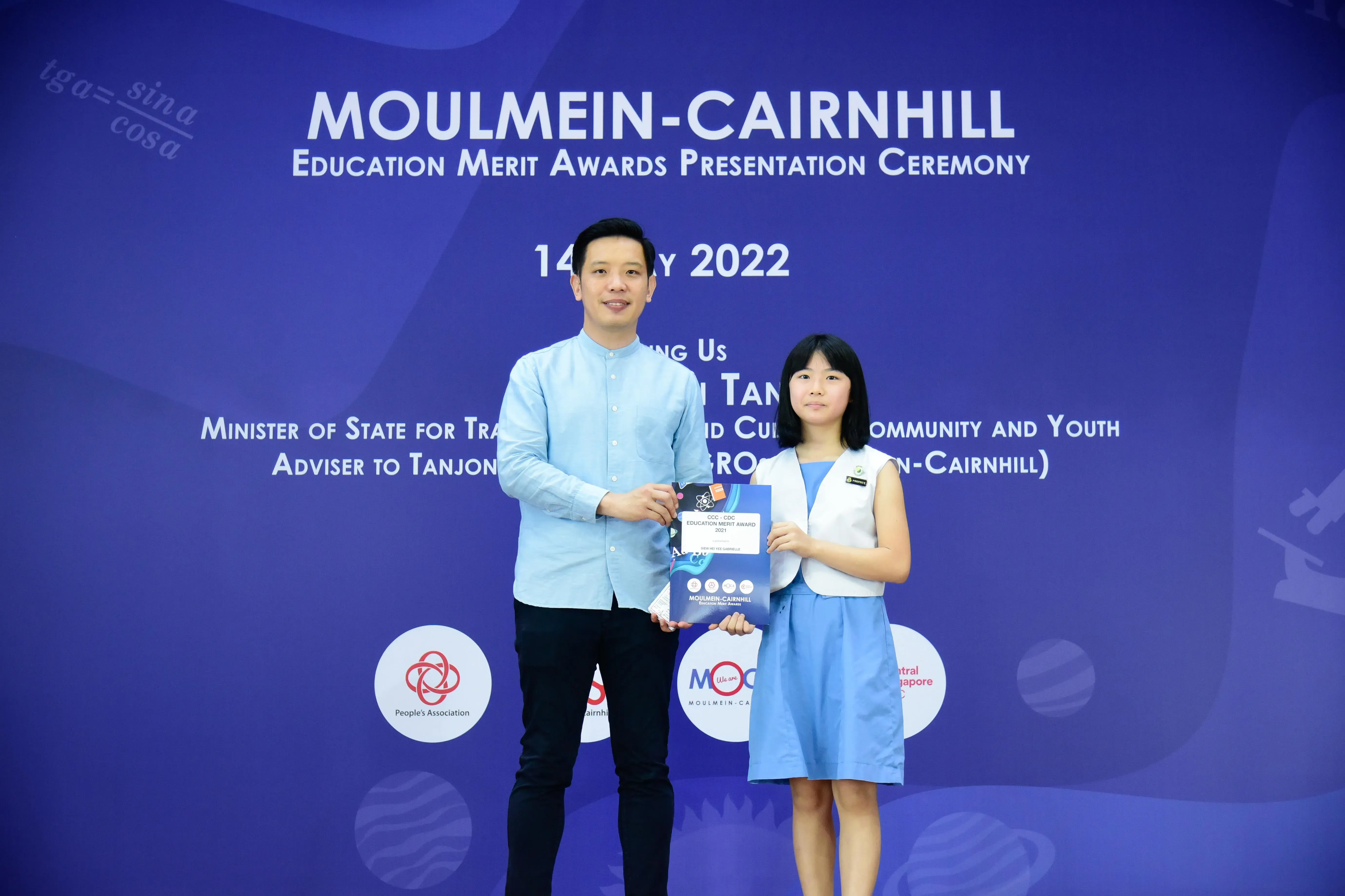 A man and a young girl hold an award certificate at the Moulmein-Cairnhill Education Merit Awards Ceremony 2022.