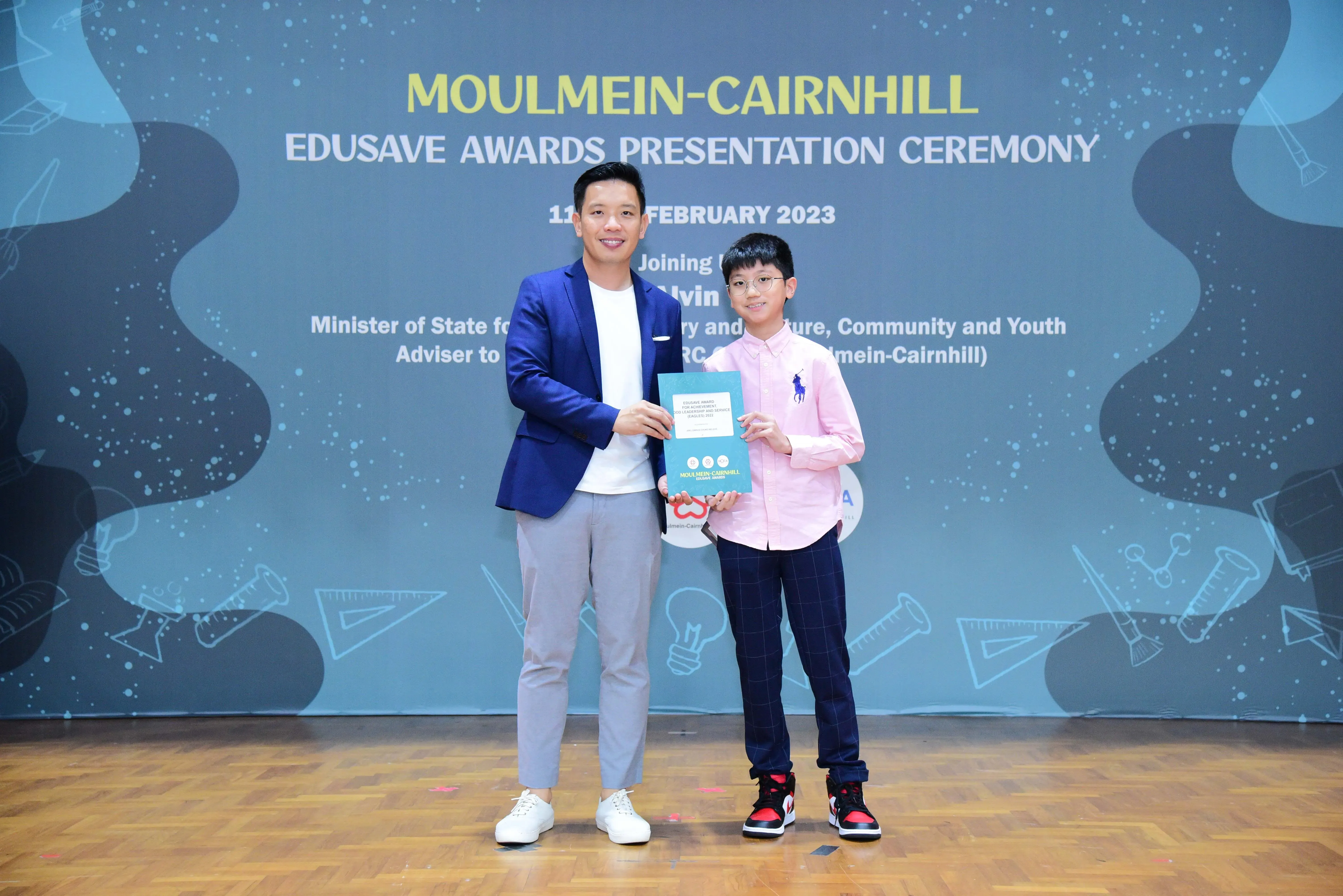 A man and a young boy hold a certificate at the Moulmein-Cairnhill Edusave Awards Ceremony, February 2023.