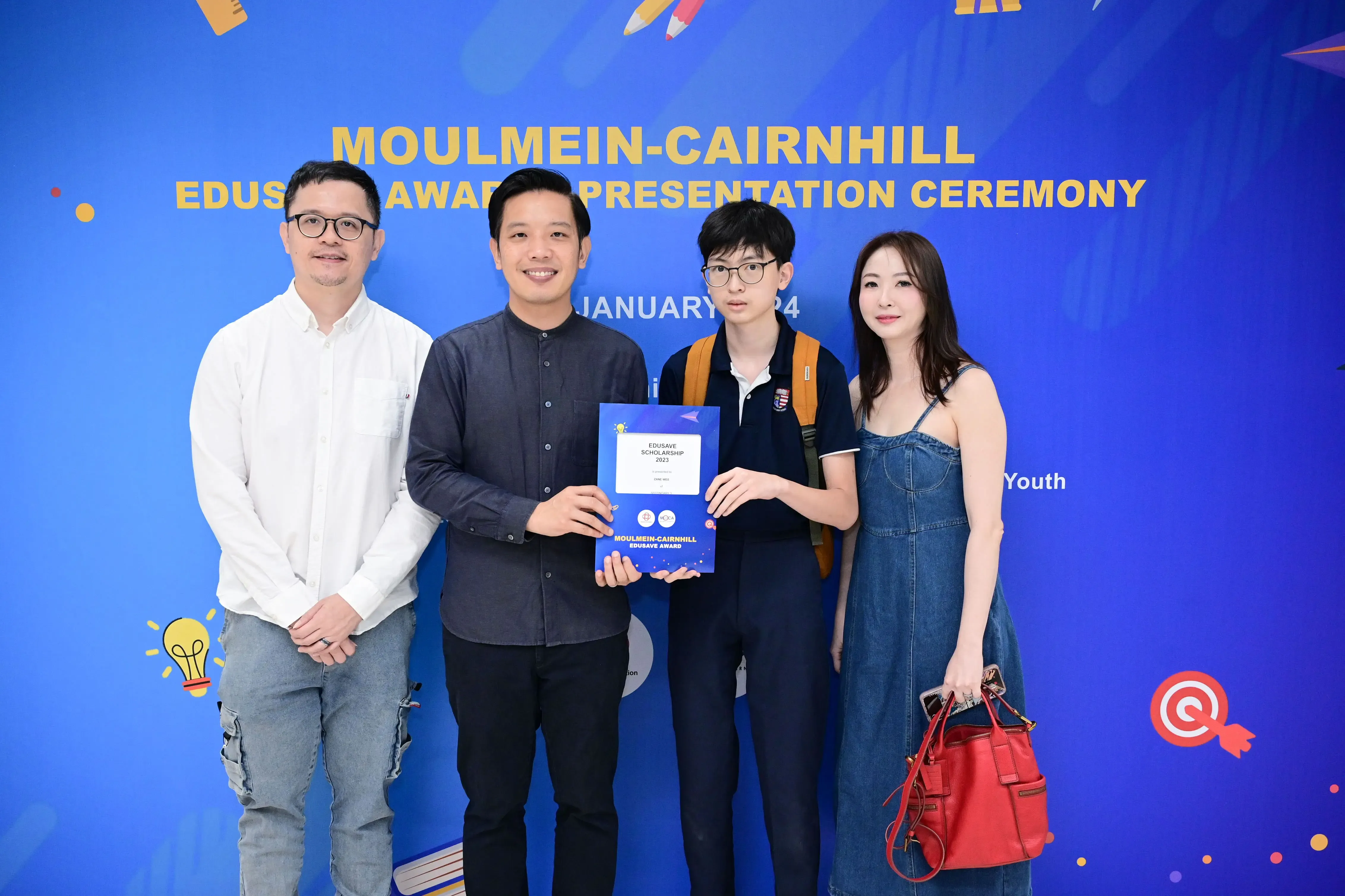Four people pose at the Moulmein-Cairnhill Edusave Award Presentation Ceremony, one holding a scholarship certificate.