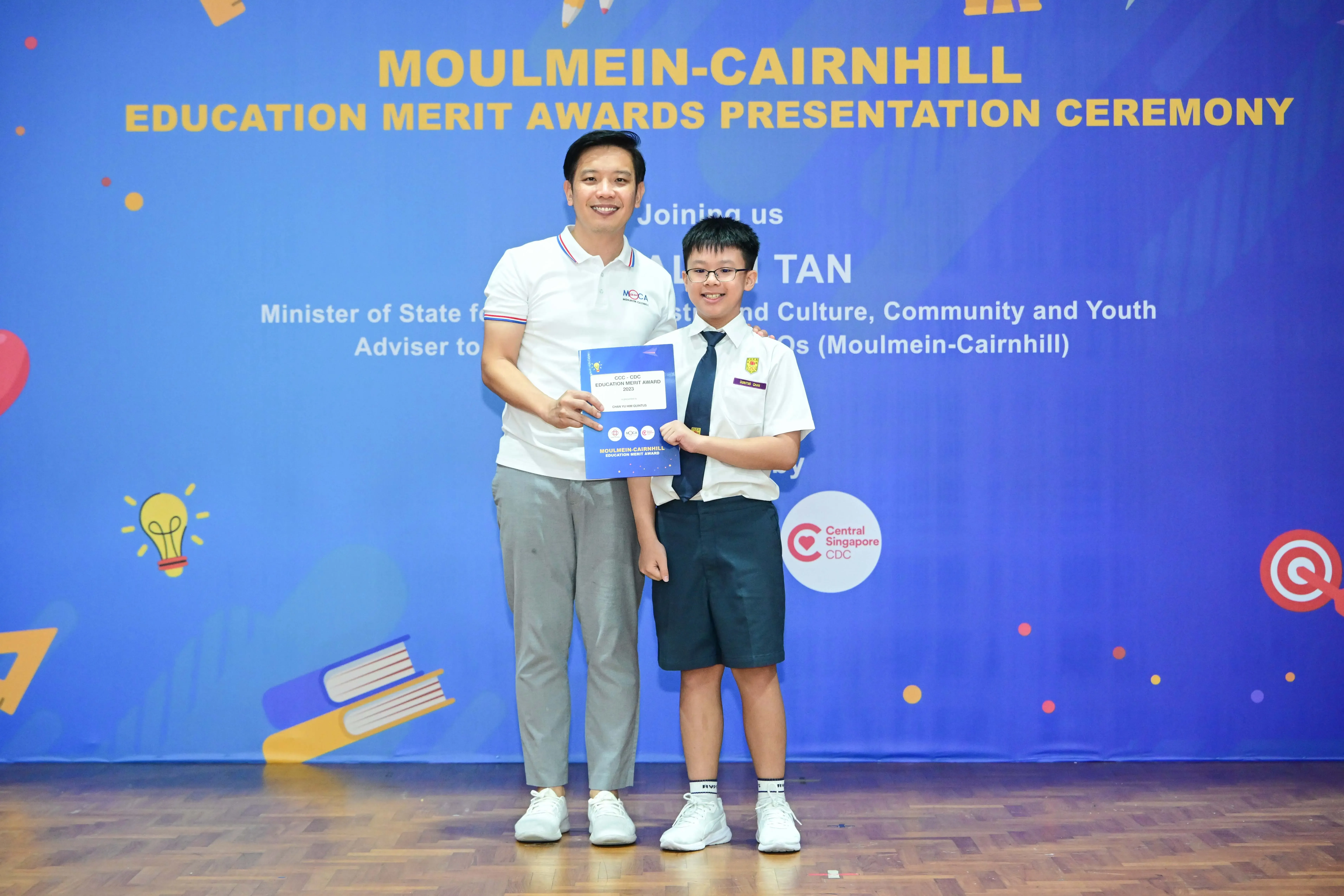 Adult and uniformed student holding an award at Moulmein-Cairnhill Education Merit Awards Presentation Ceremony.