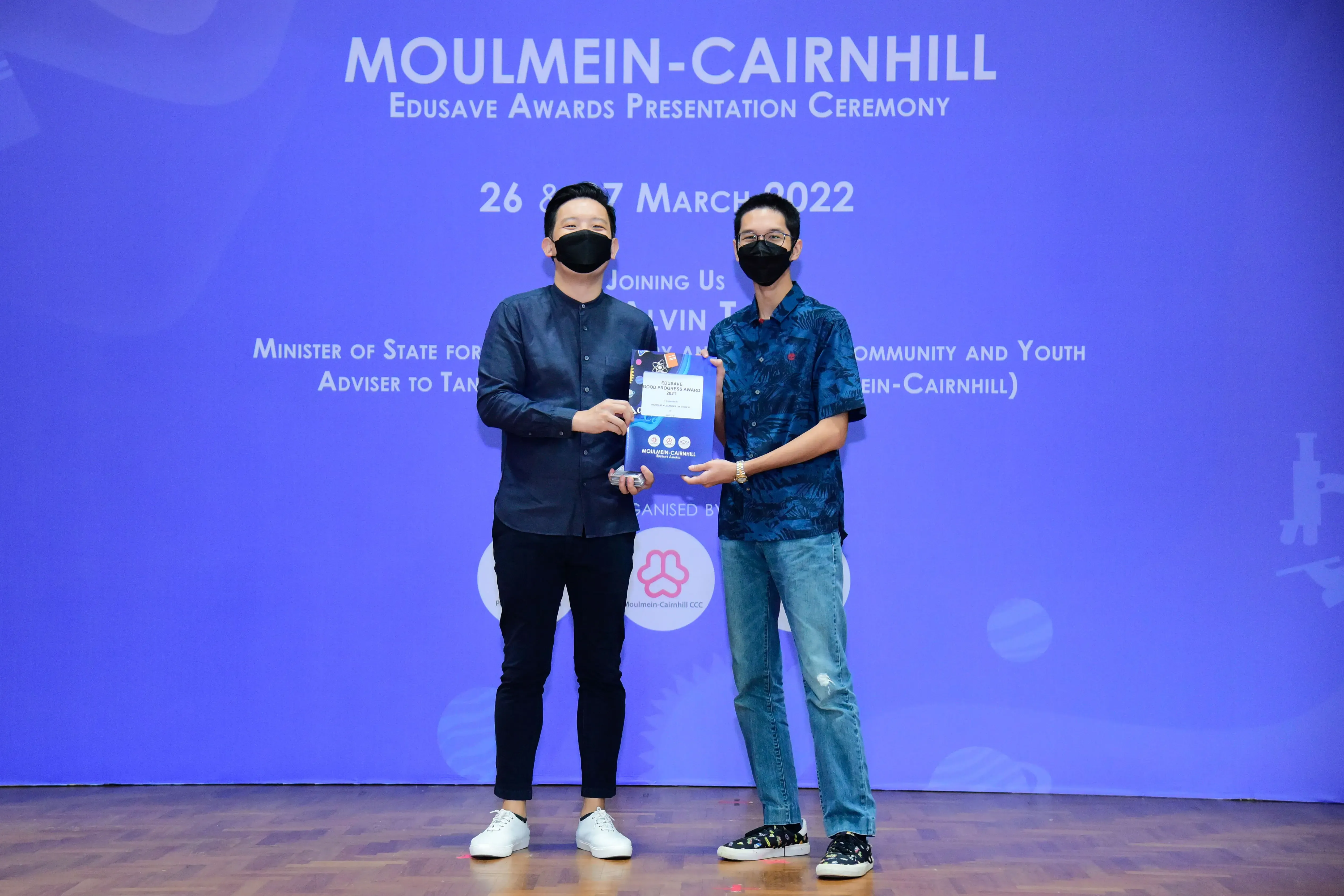 Two masked men hold an award certificate at the Moulmein-Cairnhill Edusave Awards Ceremony, March 2022.