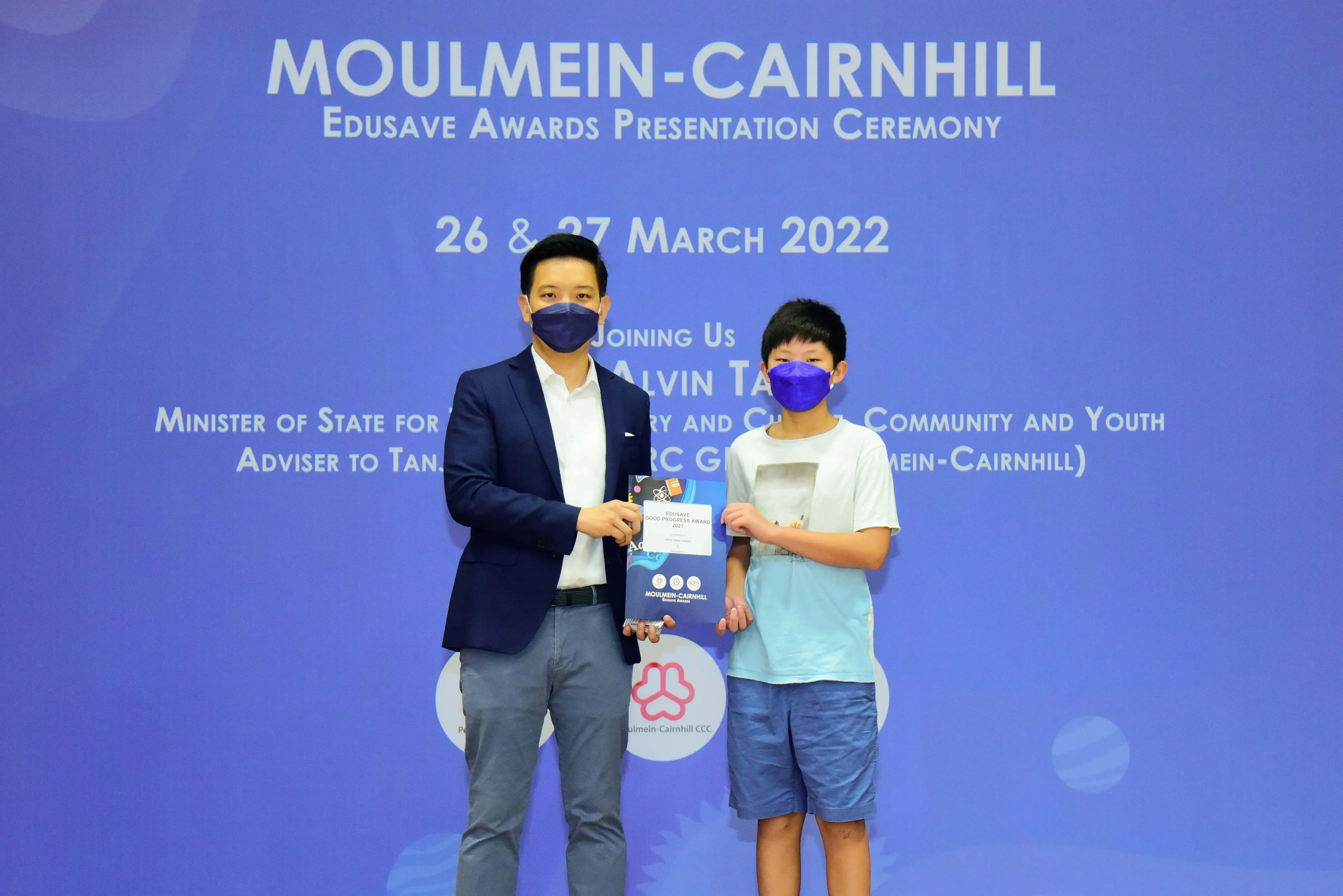 Two masked individuals hold an award certificate at the Moulmein-Cairnhill Edusave Awards Ceremony, March 2022.