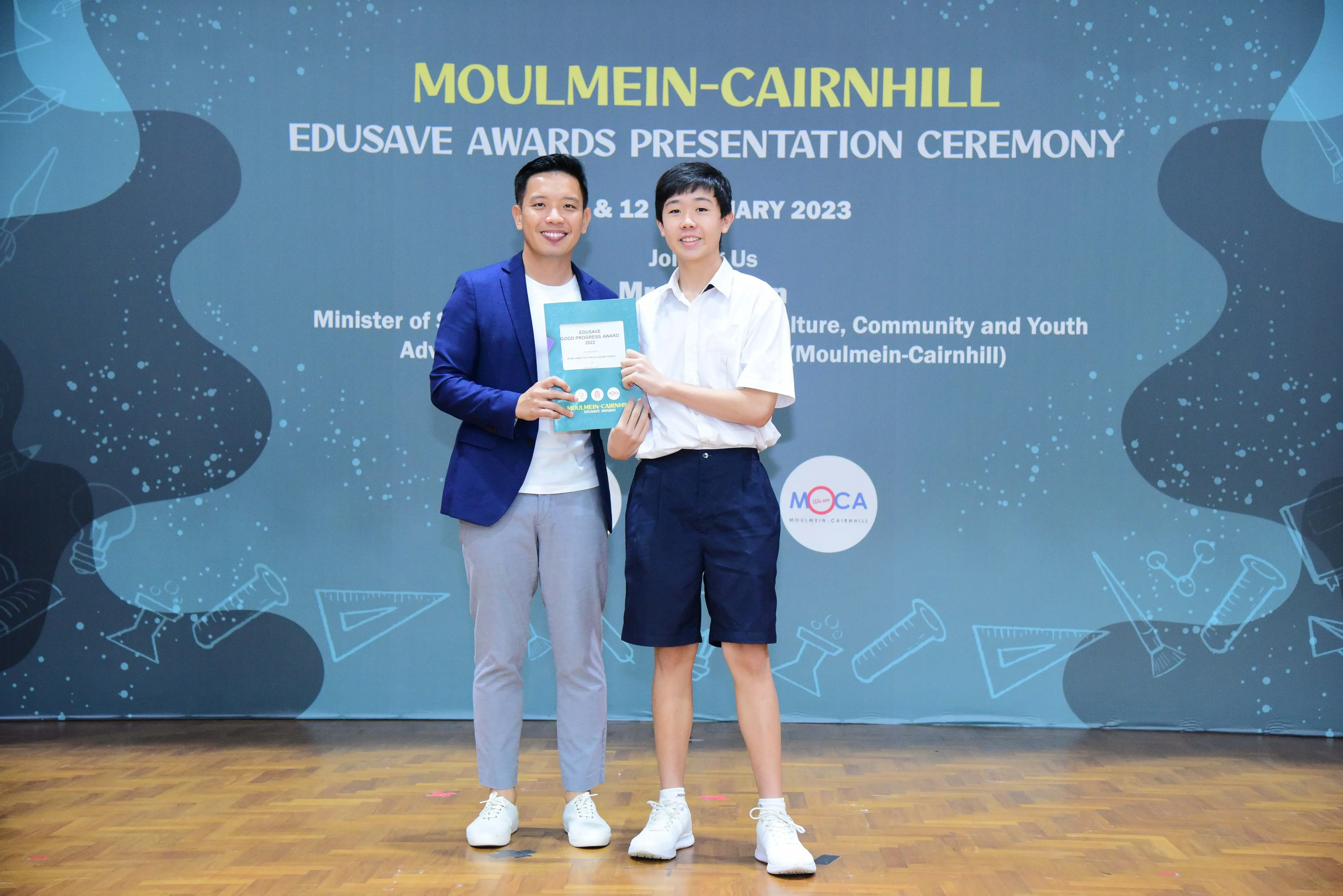 Two people smile holding an award booklet at the Moulmein-Cairnhill Edusave Awards Presentation Ceremony 2023.