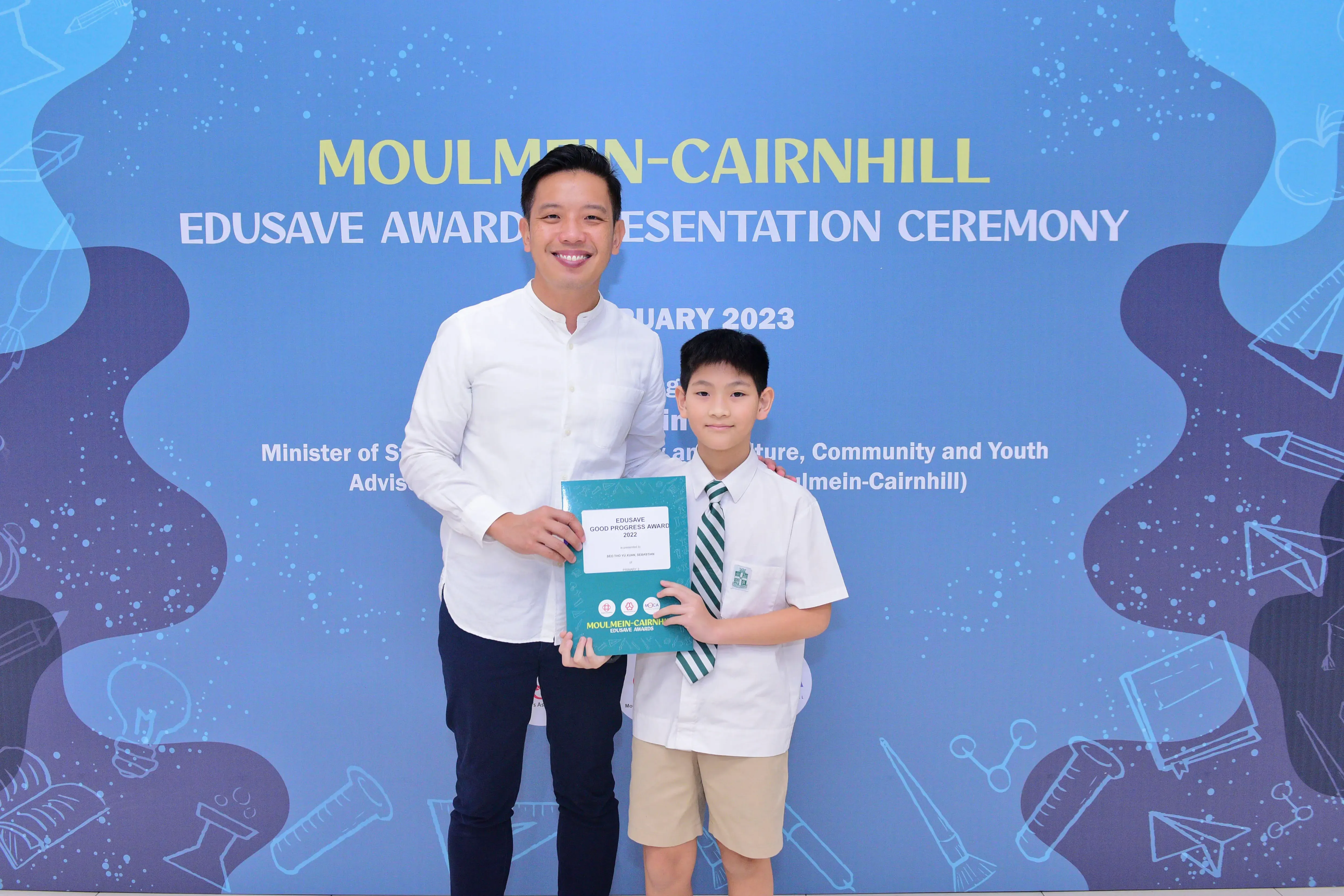 A man and a uniformed boy hold an award booklet at the Moulmein-Cairnhill Edusave Awards Presentation Ceremony 2023.