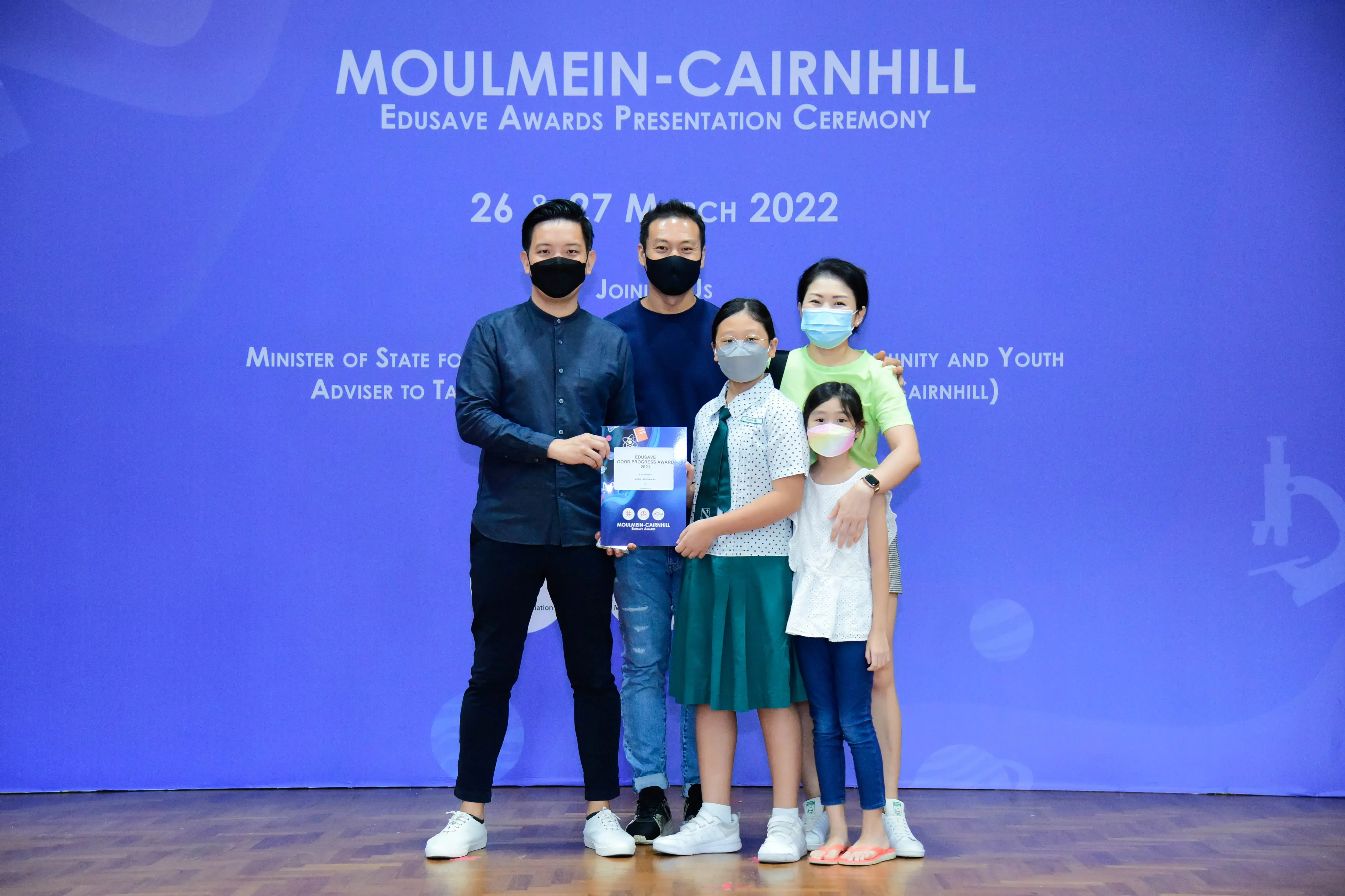Five masked people pose with an award at the Moulmein-Cairnhill Edusave Awards Presentation Ceremony, March 2022.