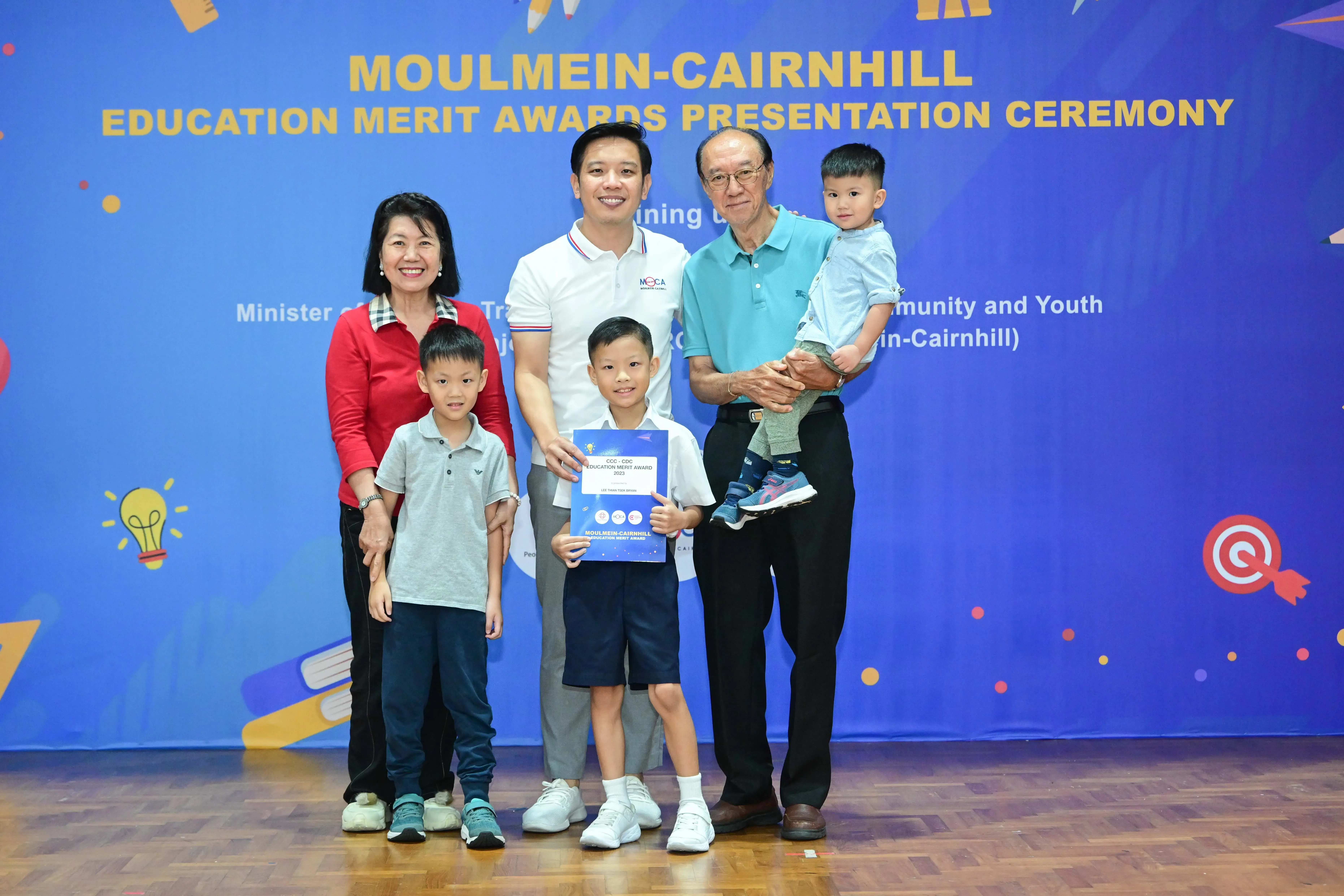 A family of five poses with a certificate at the Moulmein-Cairnhill Education Merit Awards Presentation Ceremony.