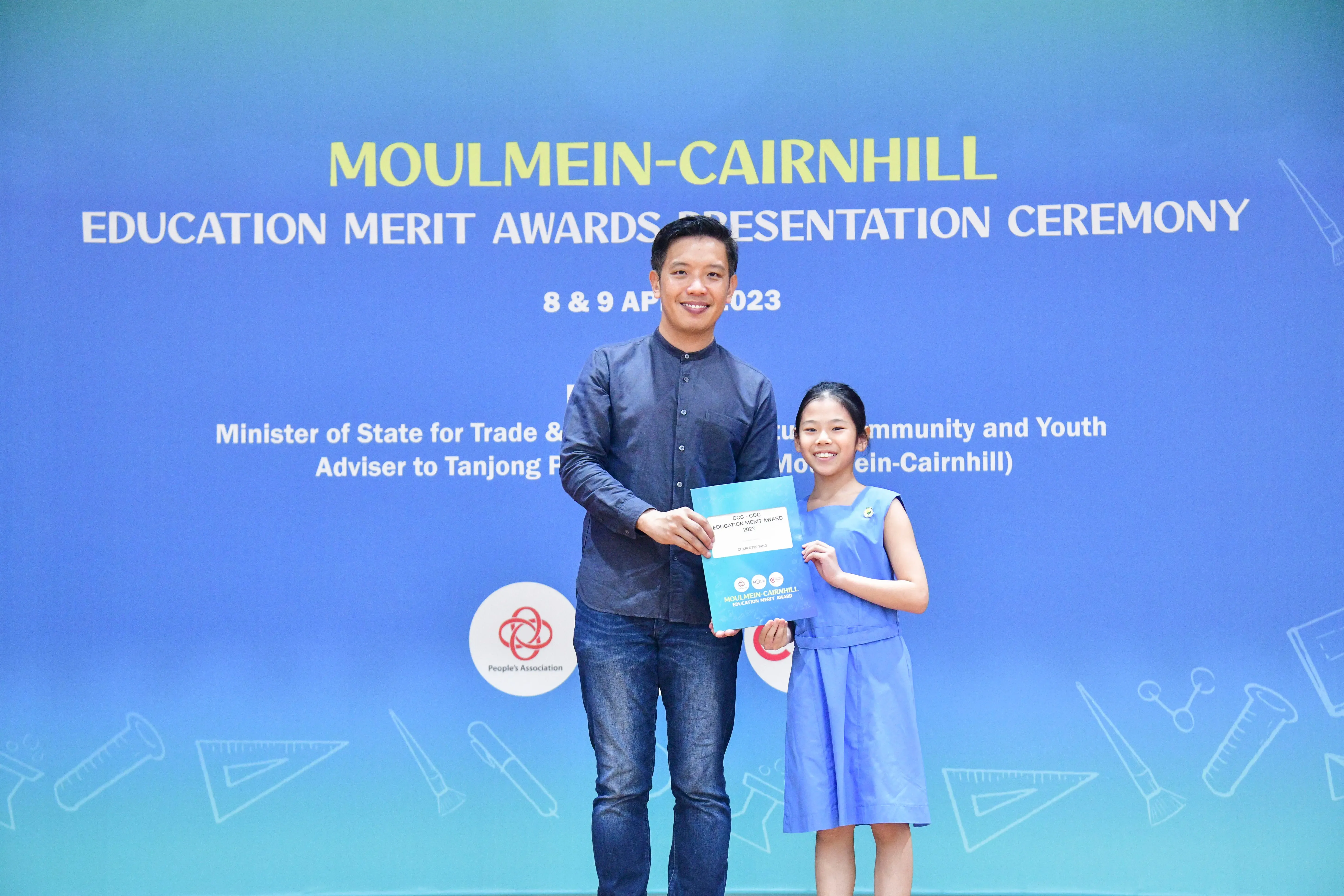 A man and a young girl hold a certificate together at the Moulmein-Cairnhill Education Merit Awards Ceremony 2023.