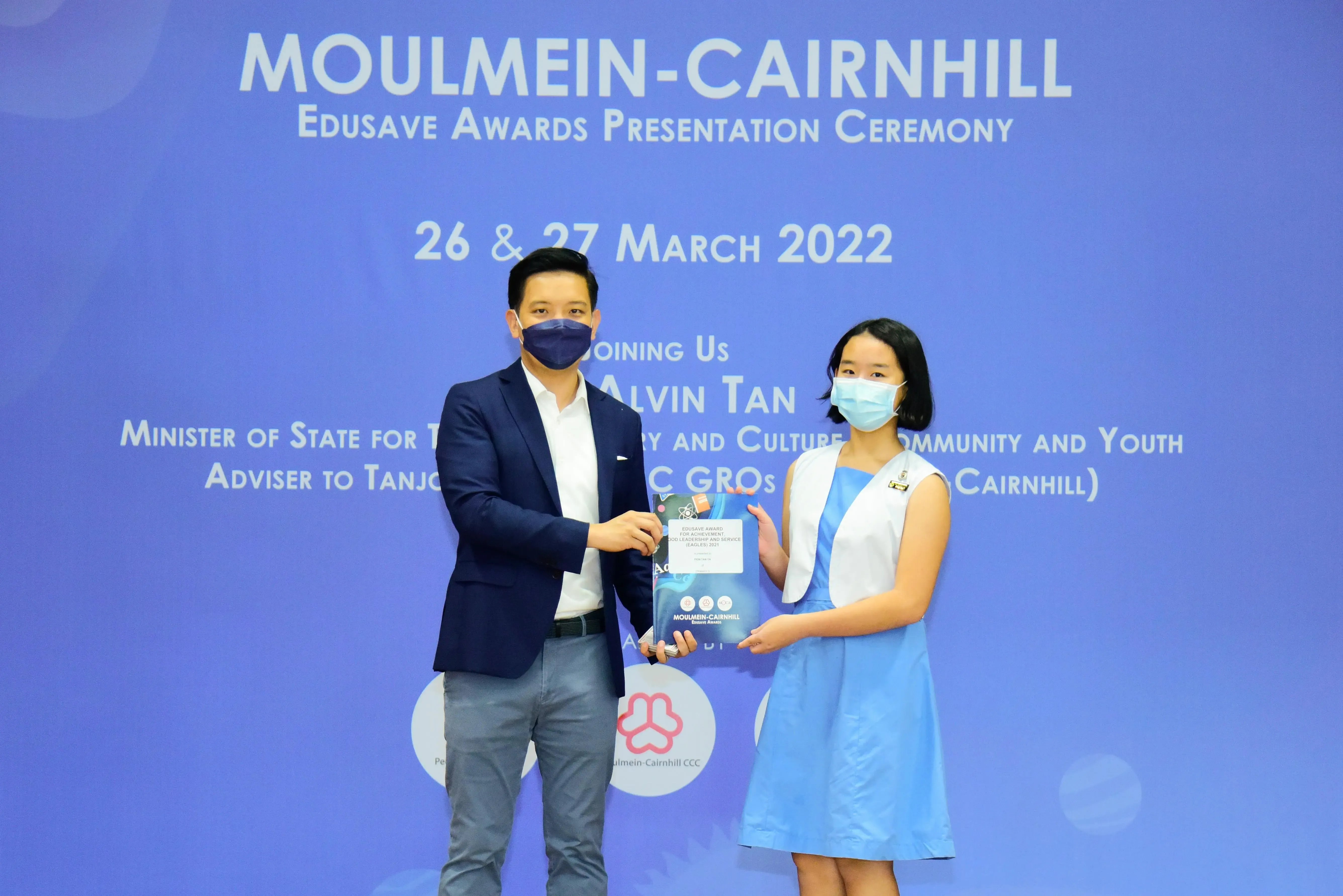Two masked people hold an award certificate at the Moulmein-Cairnhill Edusave Awards Ceremony, March 2022.