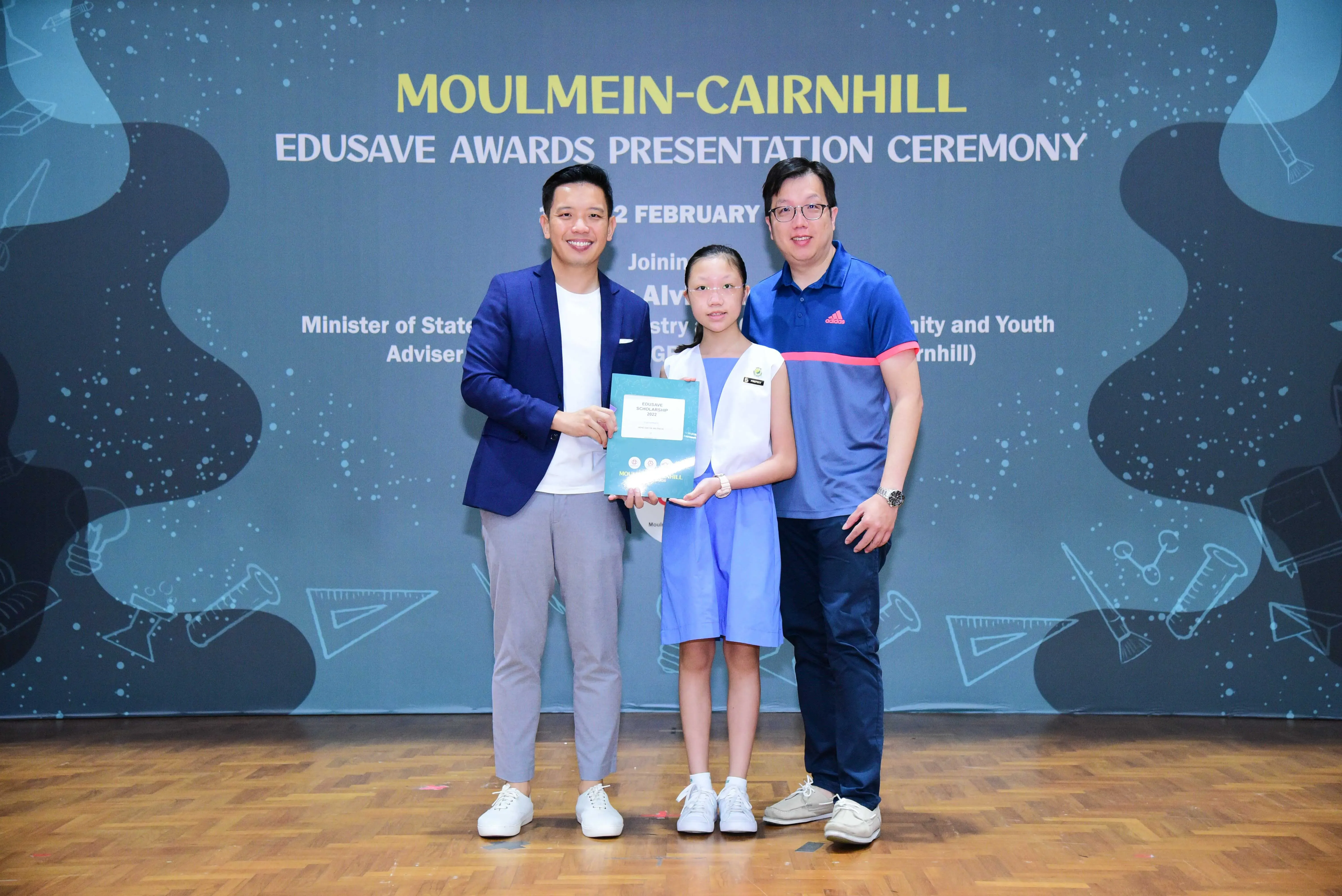 Two men and a young girl pose on stage at the Moulmein-Cairnhill Edusave Awards Presentation Ceremony.
