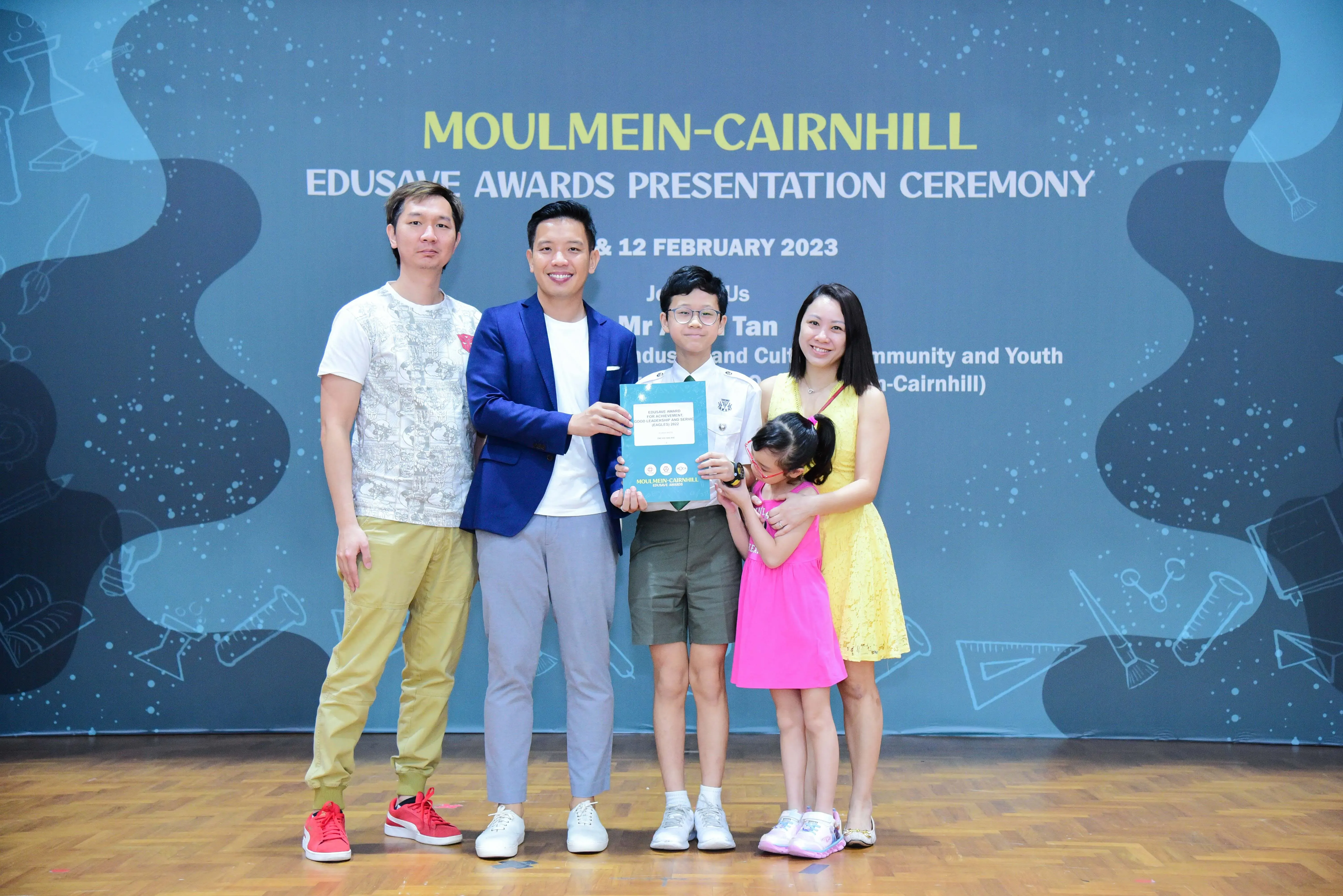 Four adults and two children pose at the Moulmein-Cairnhill Edusave Awards Presentation Ceremony on 12 February 2023.
