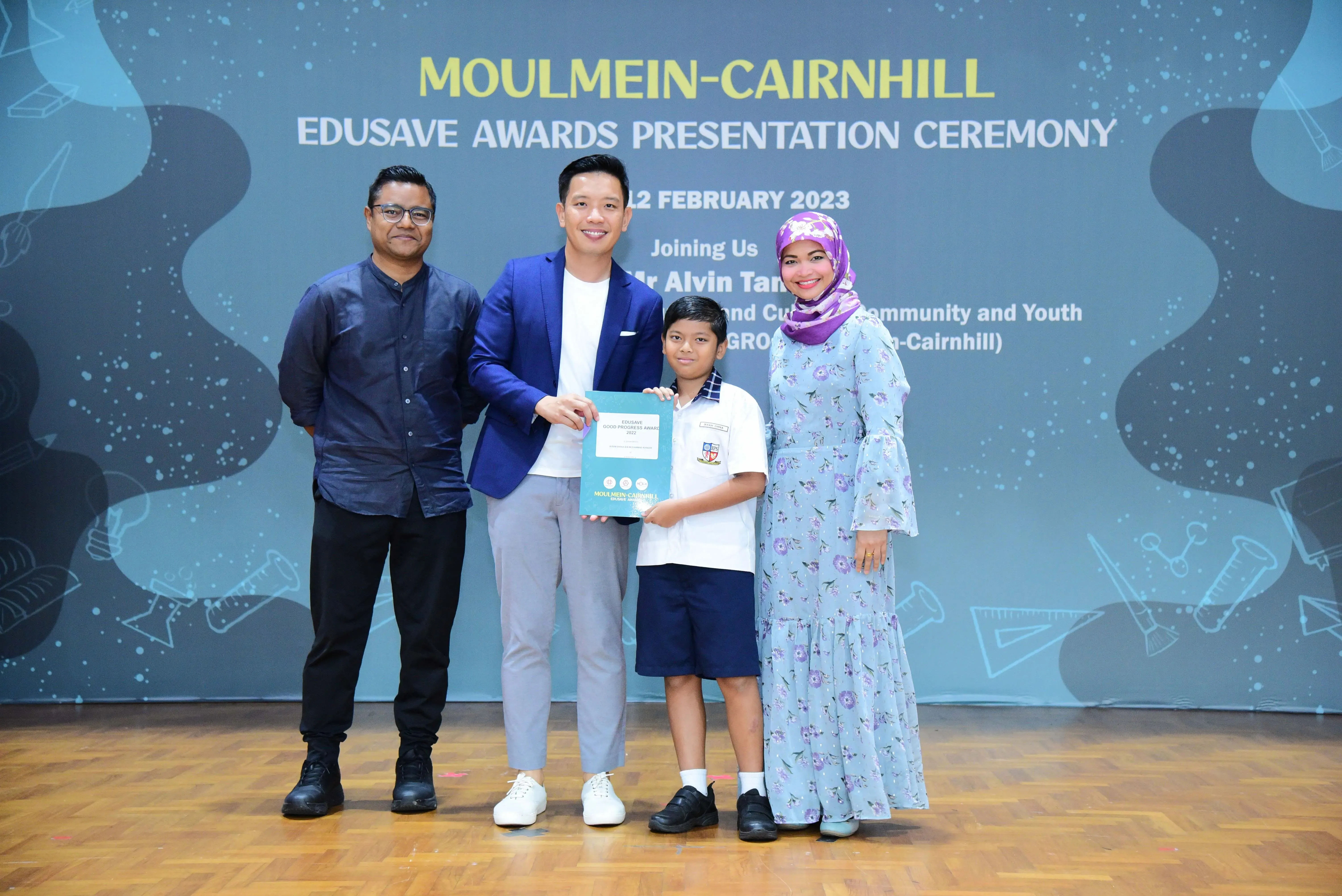 Three adults and a young student pose on stage holding an award at the Moulmein-Cairnhill Edusave Awards Ceremony 2023.